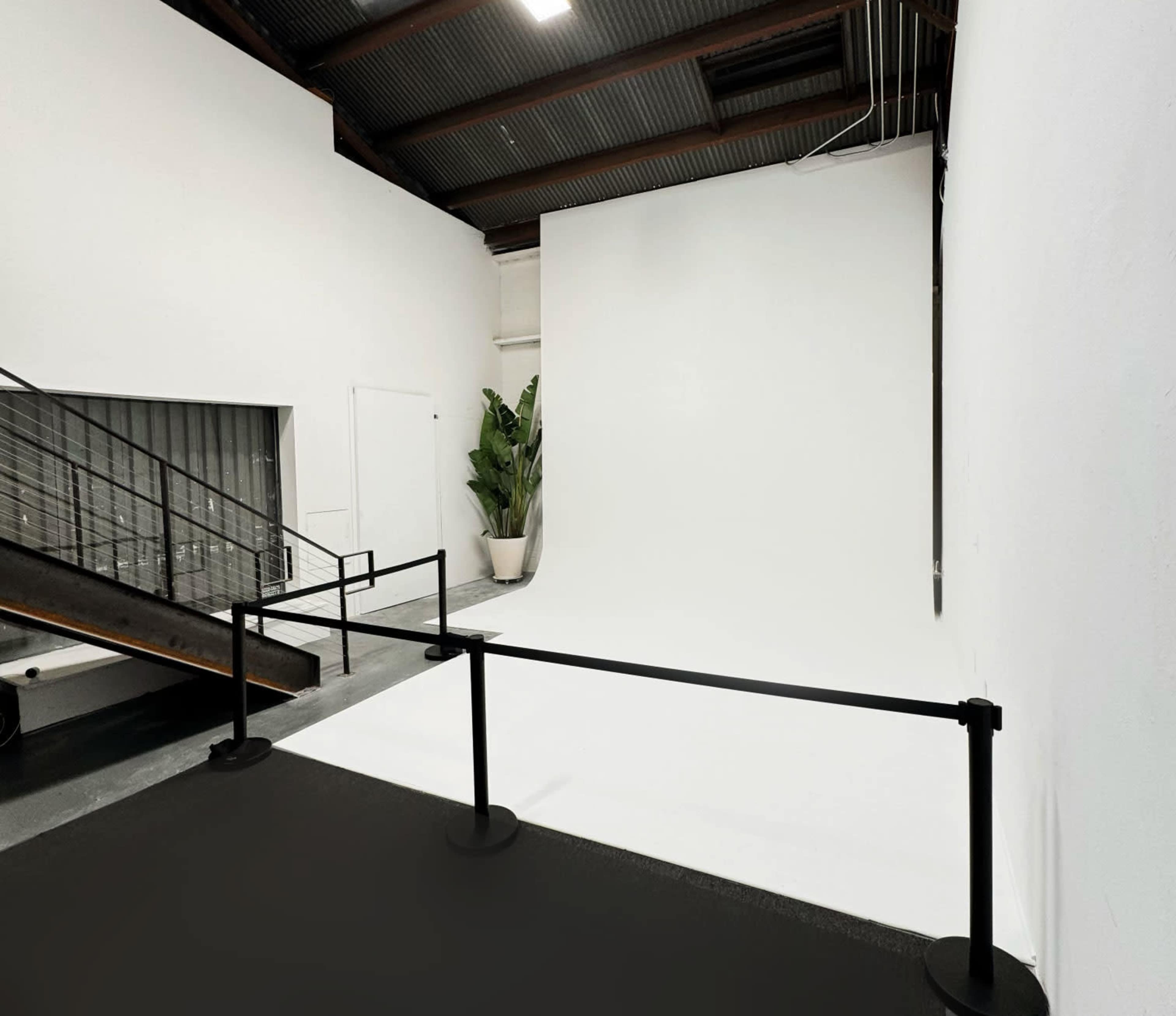 A spacious photography studio with a large white backdrop and a staircase leading to an upper level.