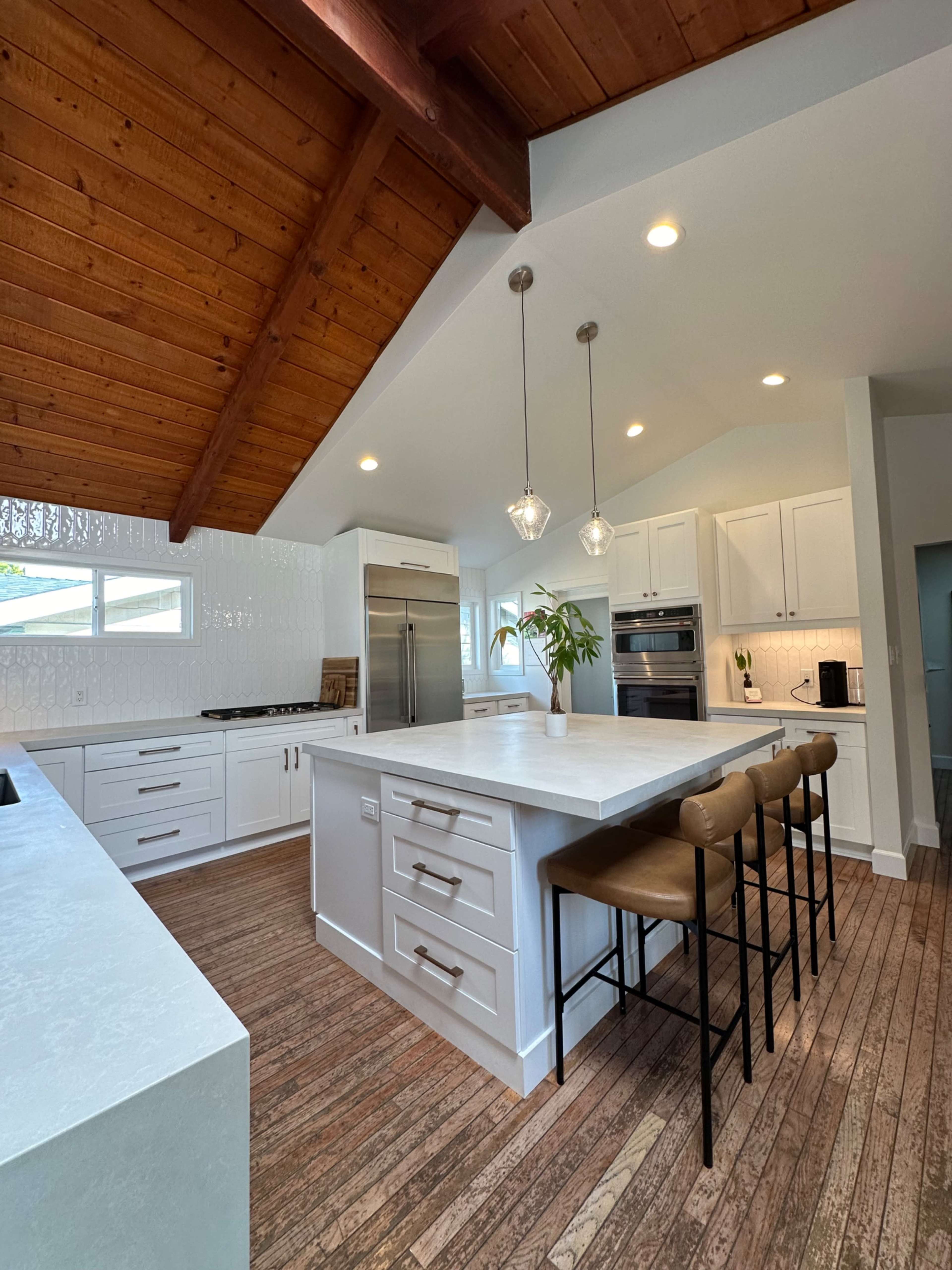 A modern kitchen with a large island, white cabinetry, stainless steel appliances, and a vaulted wooden ceiling.