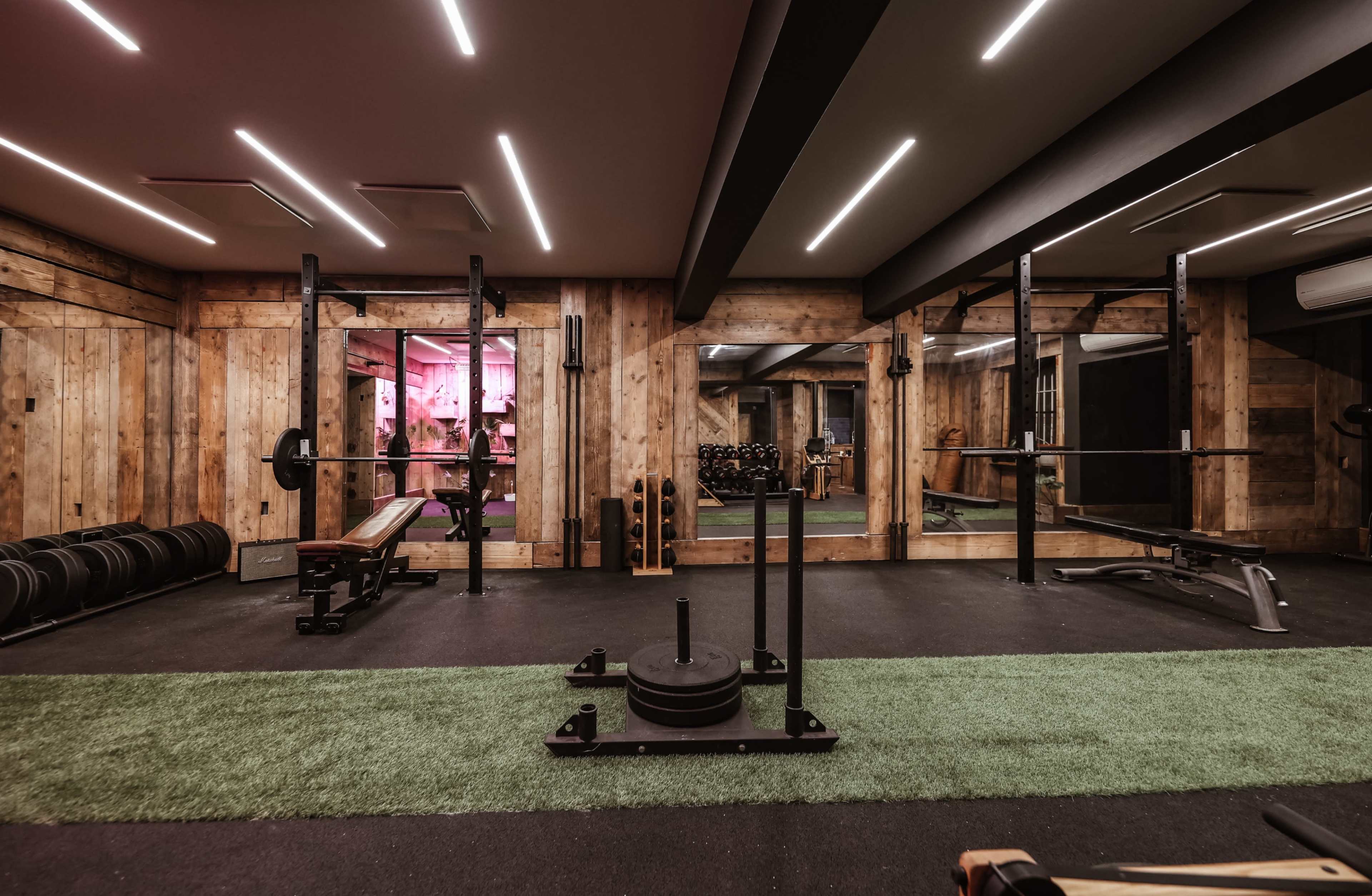 The image shows a modern gym interior featuring weightlifting equipment, mirrors, and turf flooring under dim lighting.