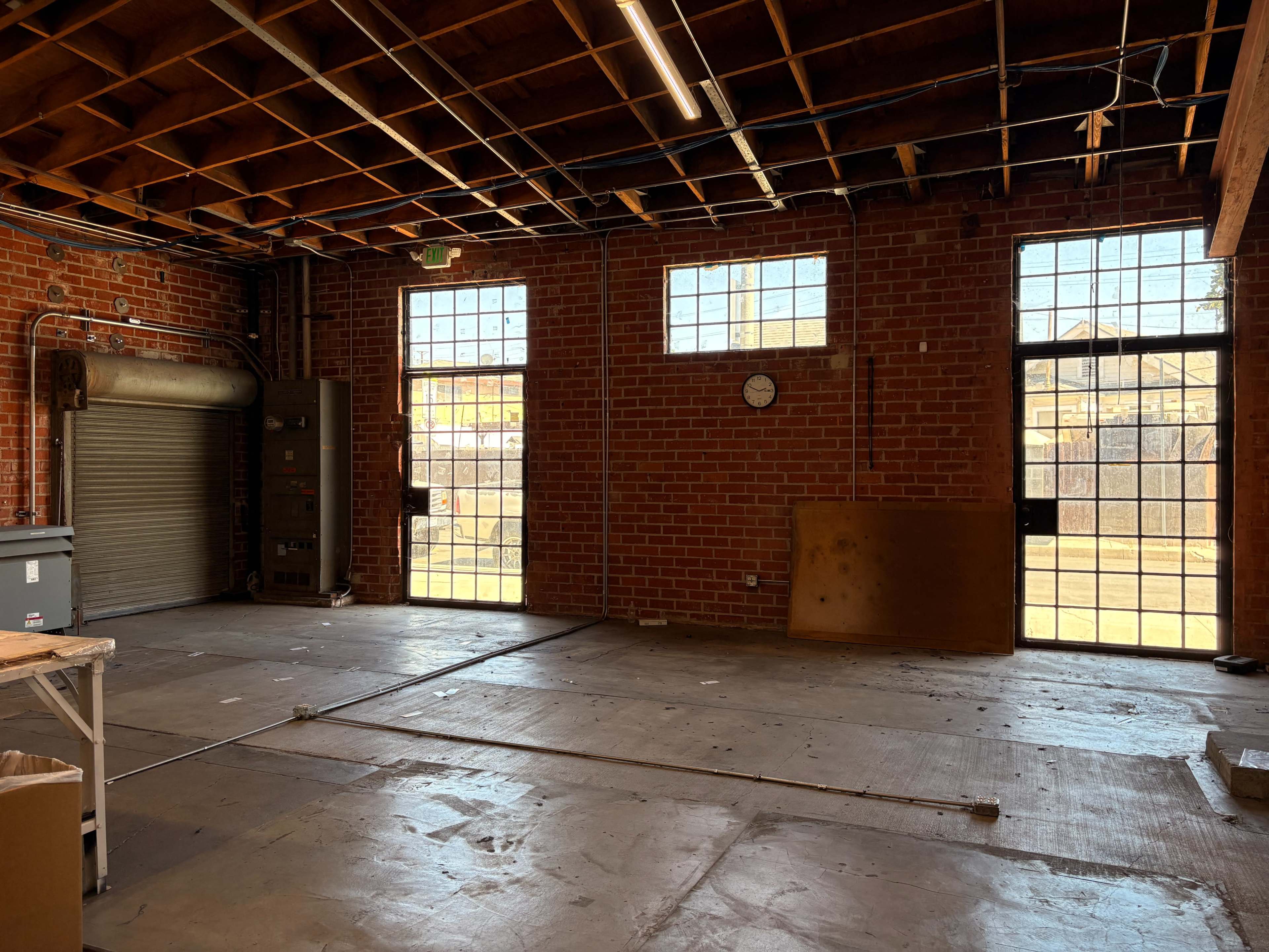 The image shows an empty industrial space with brick walls, large windows, and a roll-up door.