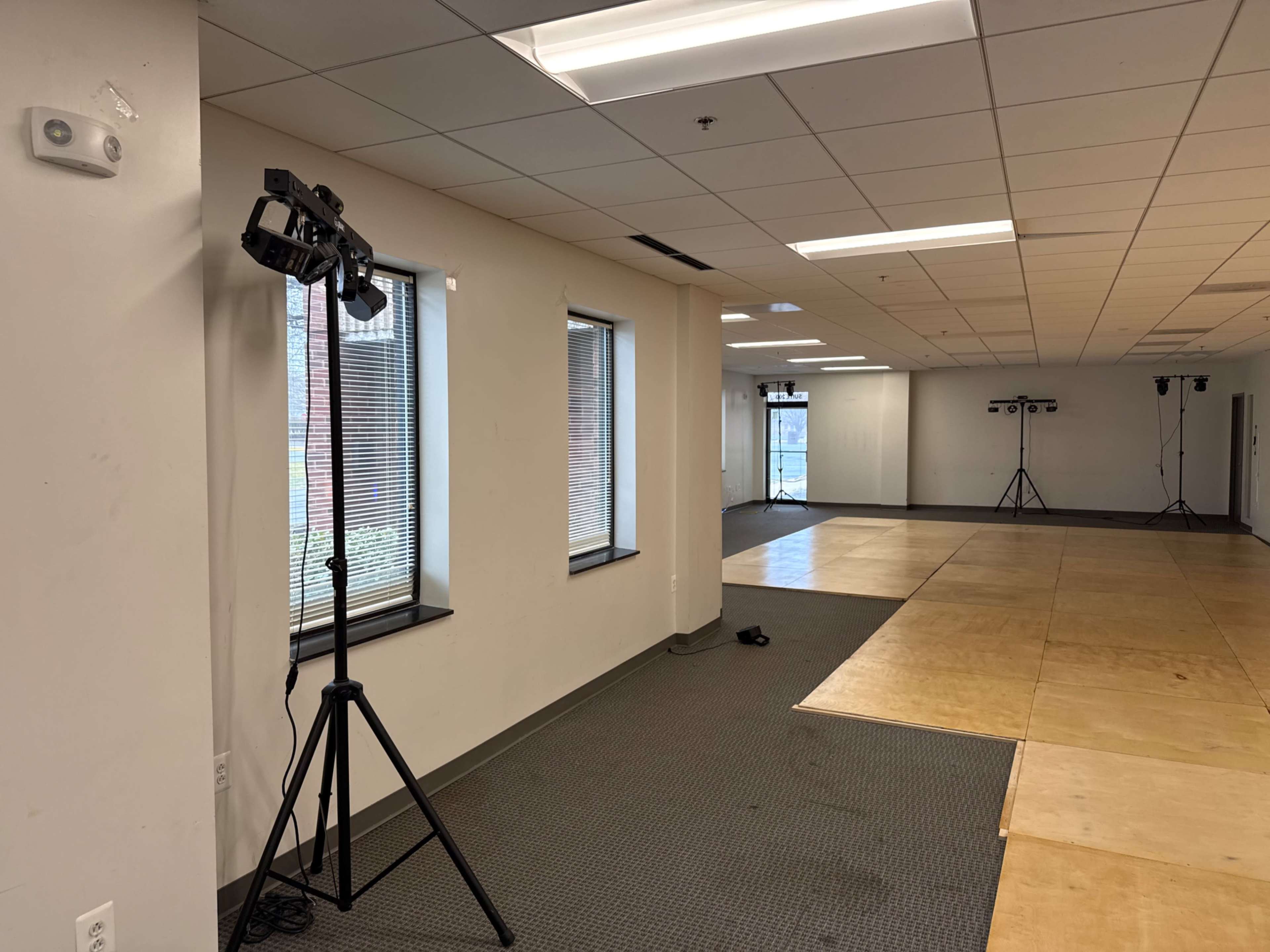 The image shows an empty room with two lighting stands positioned on opposite sides and a section of the floor covered in wooden panels.