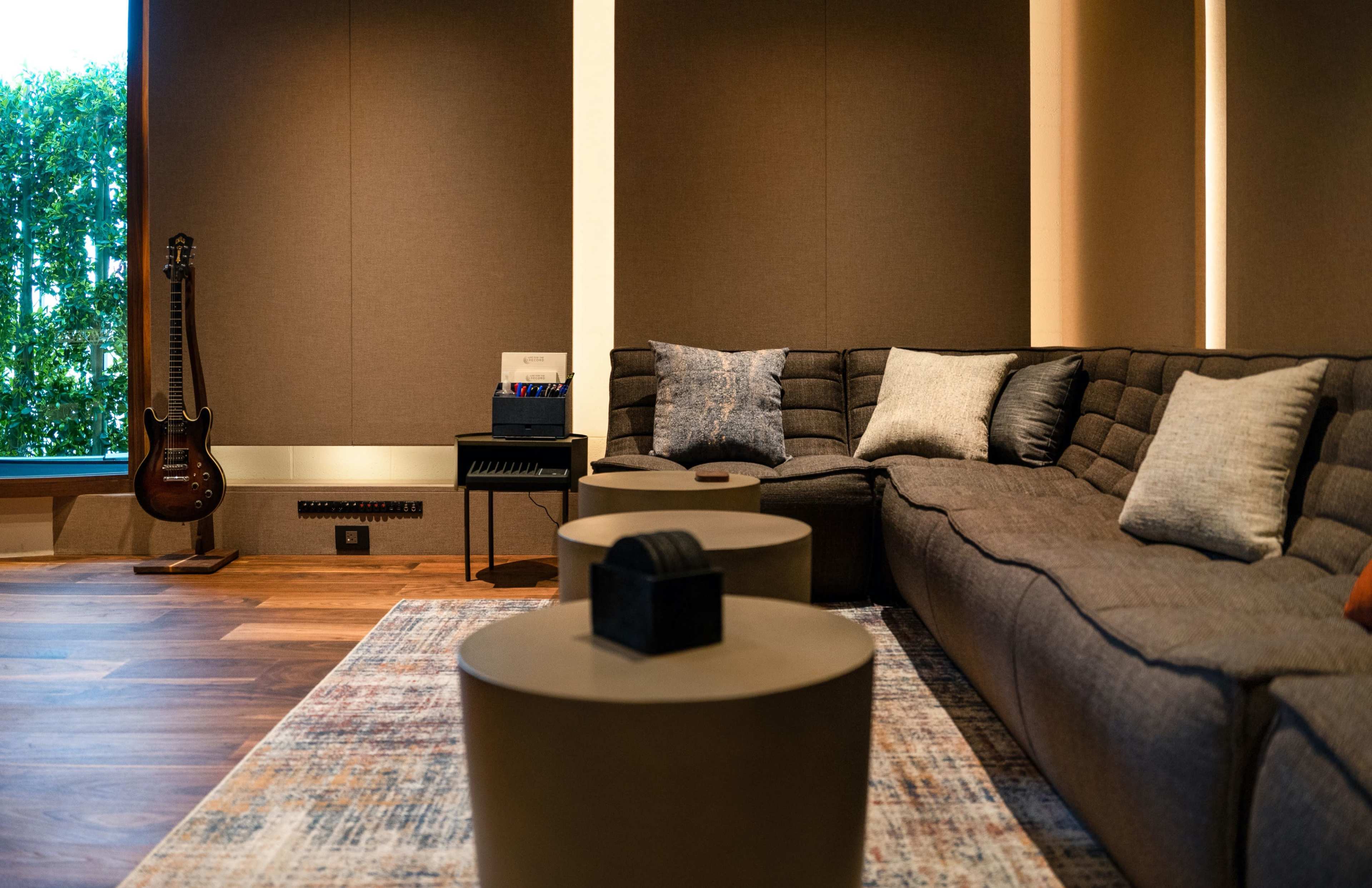A modern living room with a large sectional sofa, two round coffee tables, and a guitar leaning against the wall.