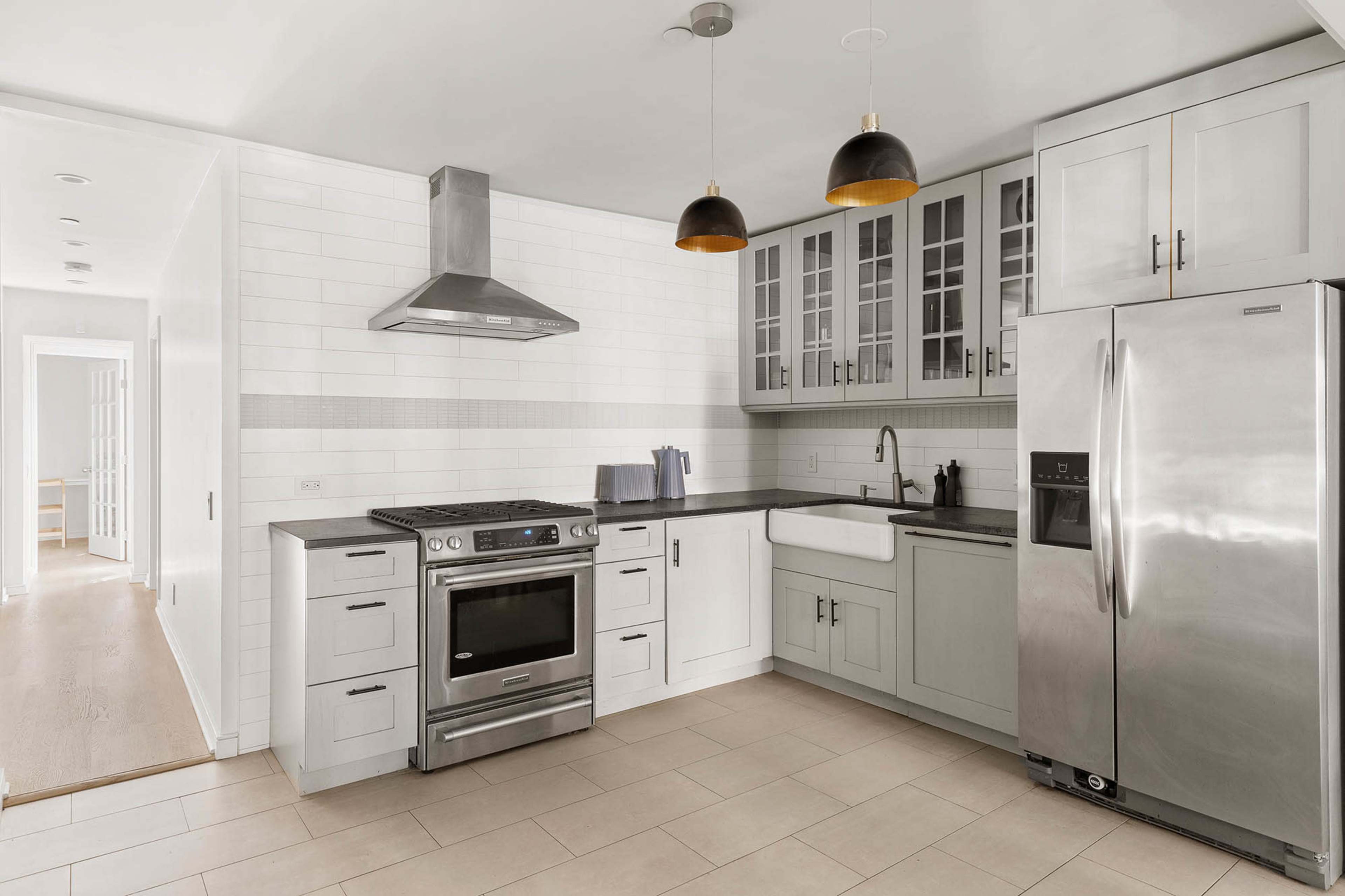 The kitchen features stainless steel appliances, a white subway tile backsplash, and gray cabinets with glass inserts.