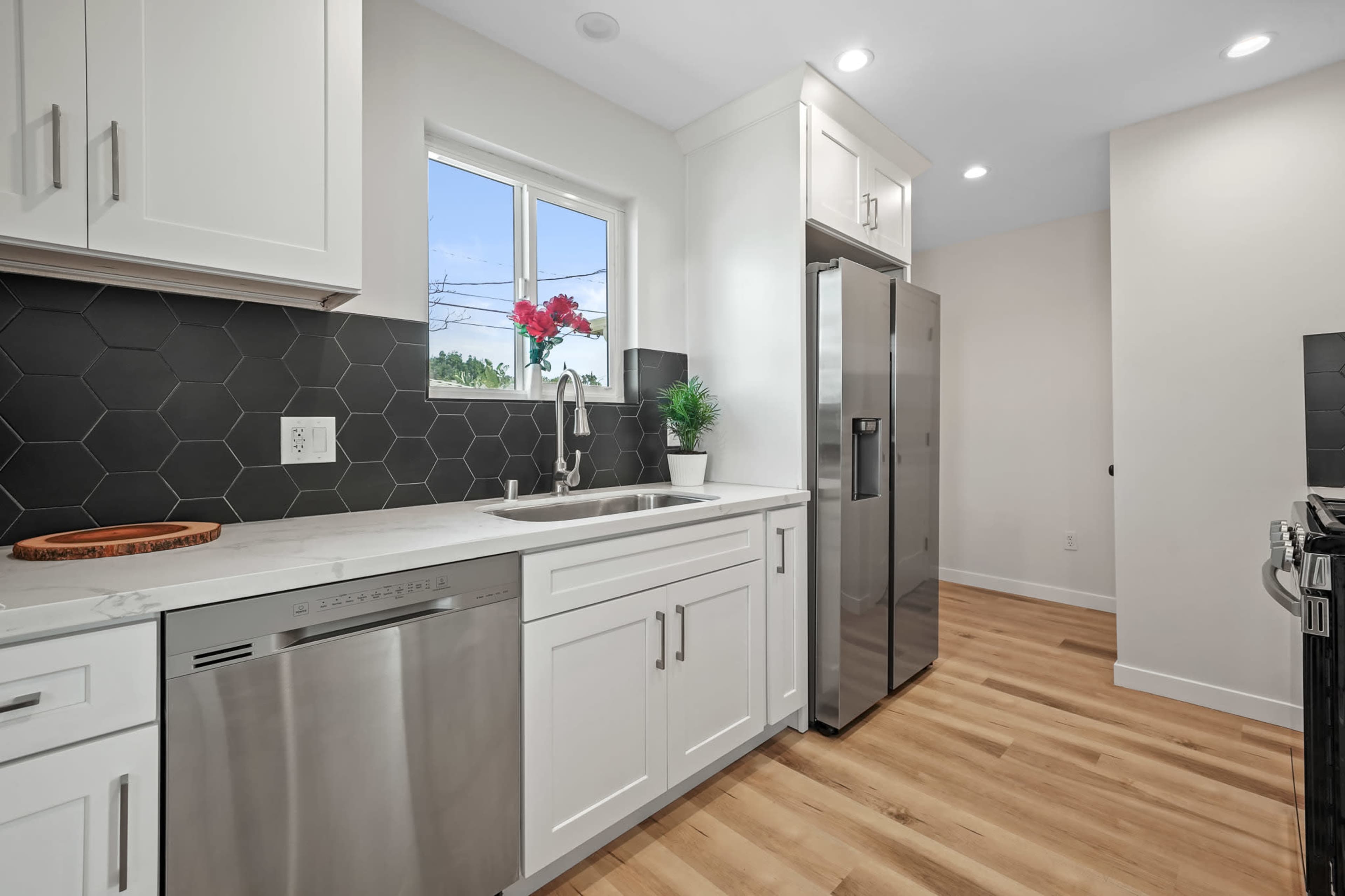 A modern kitchen features white cabinetry, stainless steel appliances, and a hexagonal tile backsplash.
