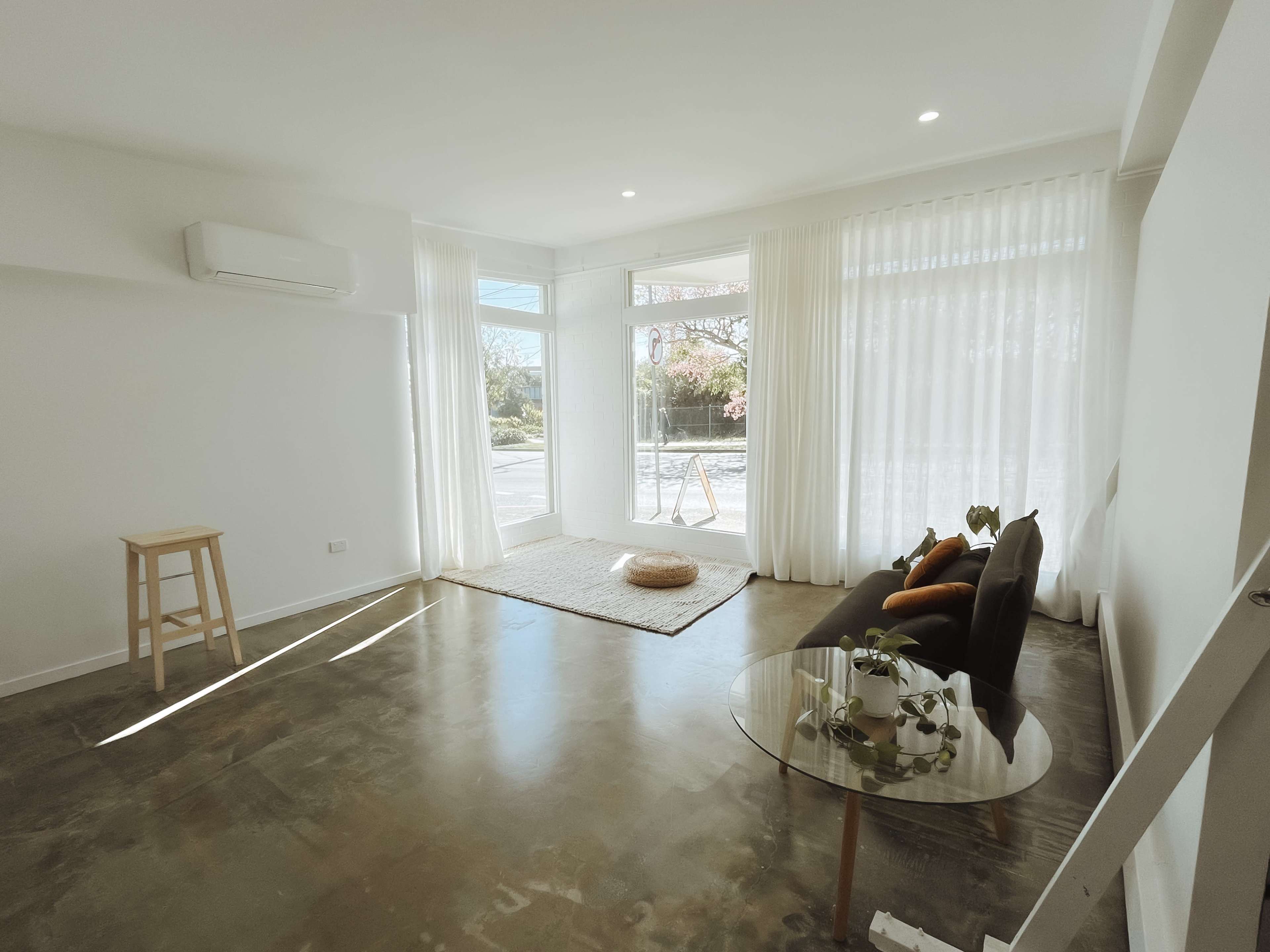 The image depicts a modern living room with large windows, minimalistic furniture, and polished concrete flooring.