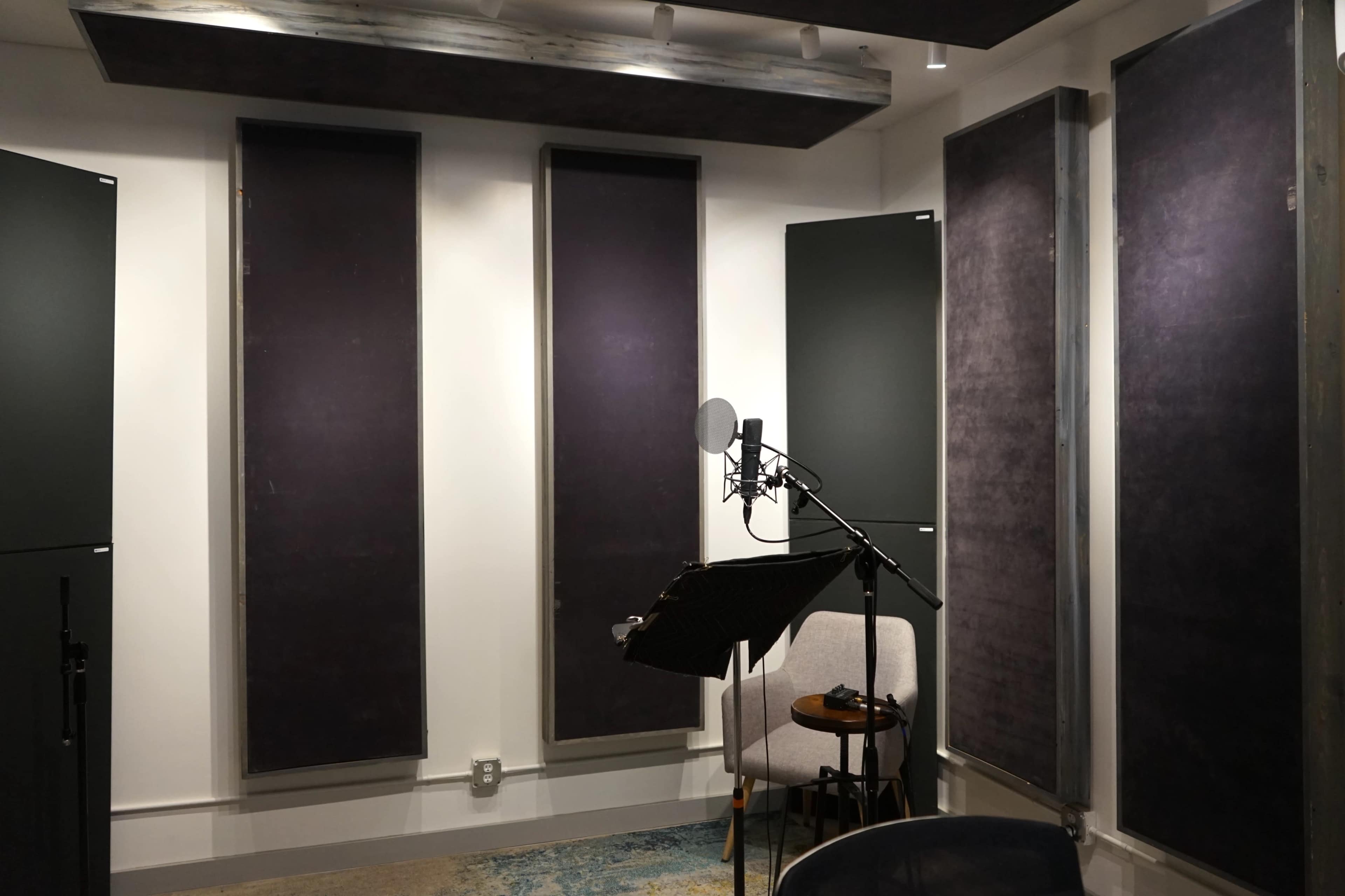 A sound recording studio with padded wall panels, a microphone on a stand, a music stand, and a chair.