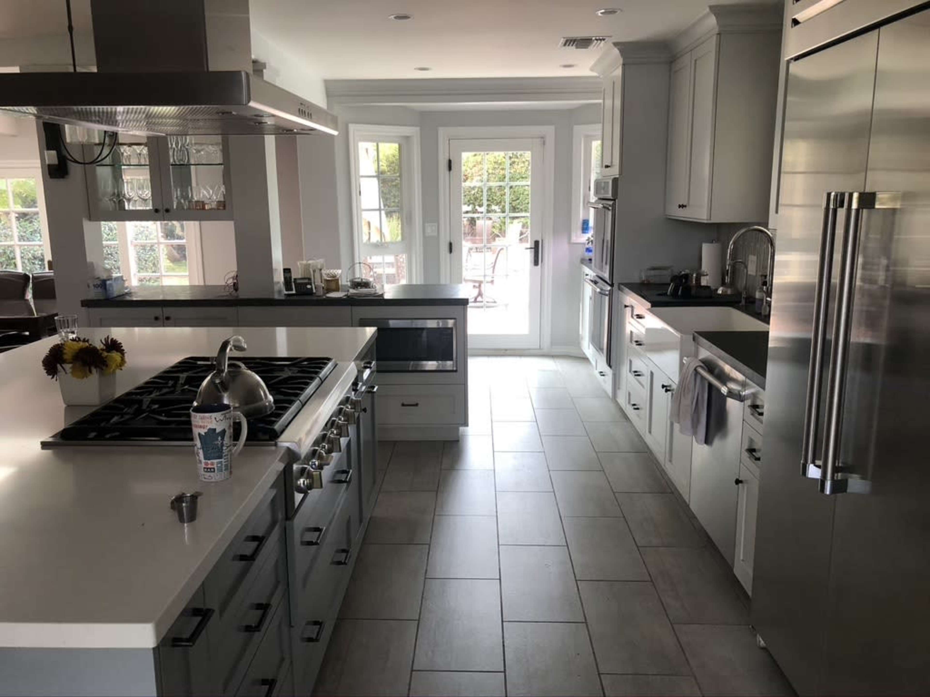 A modern kitchen features gray cabinetry, stainless steel appliances, and a large island, with a view of a patio through sliding glass doors.