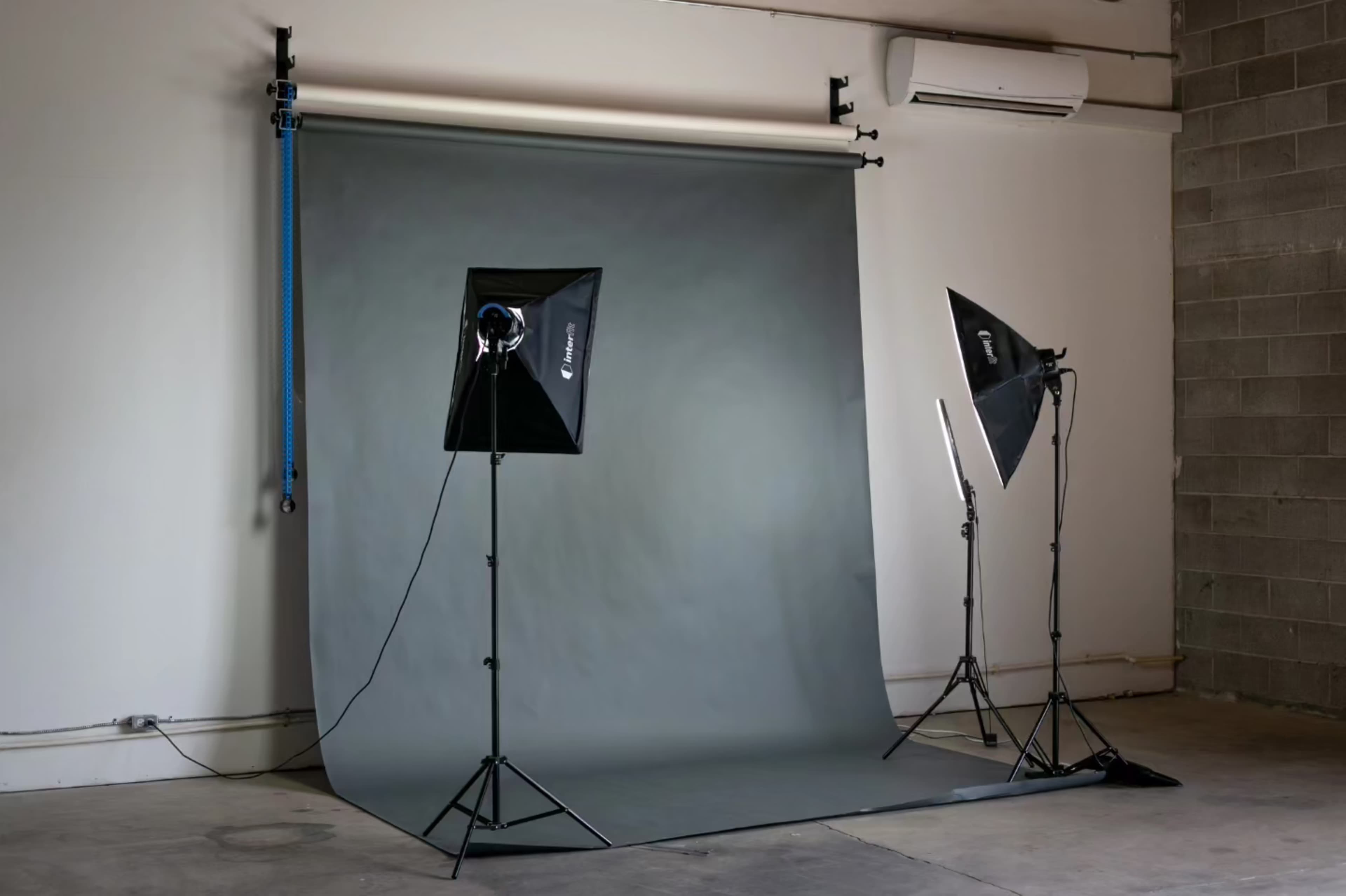 The image shows a photography studio setup with a gray backdrop and two softbox lights on stands.