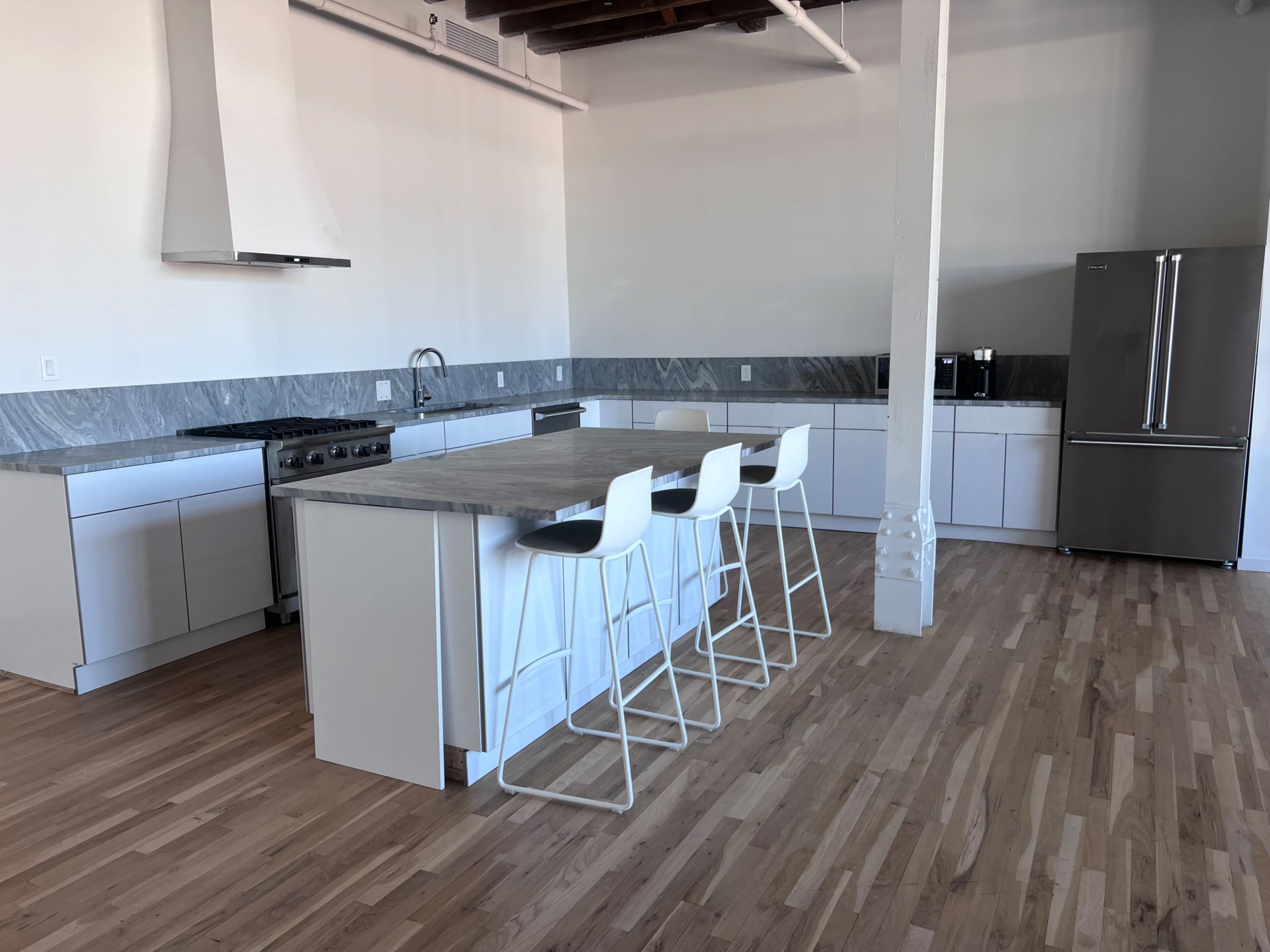 The image shows a modern kitchen with a large island, white cabinetry, stainless steel appliances, and a wooden floor.