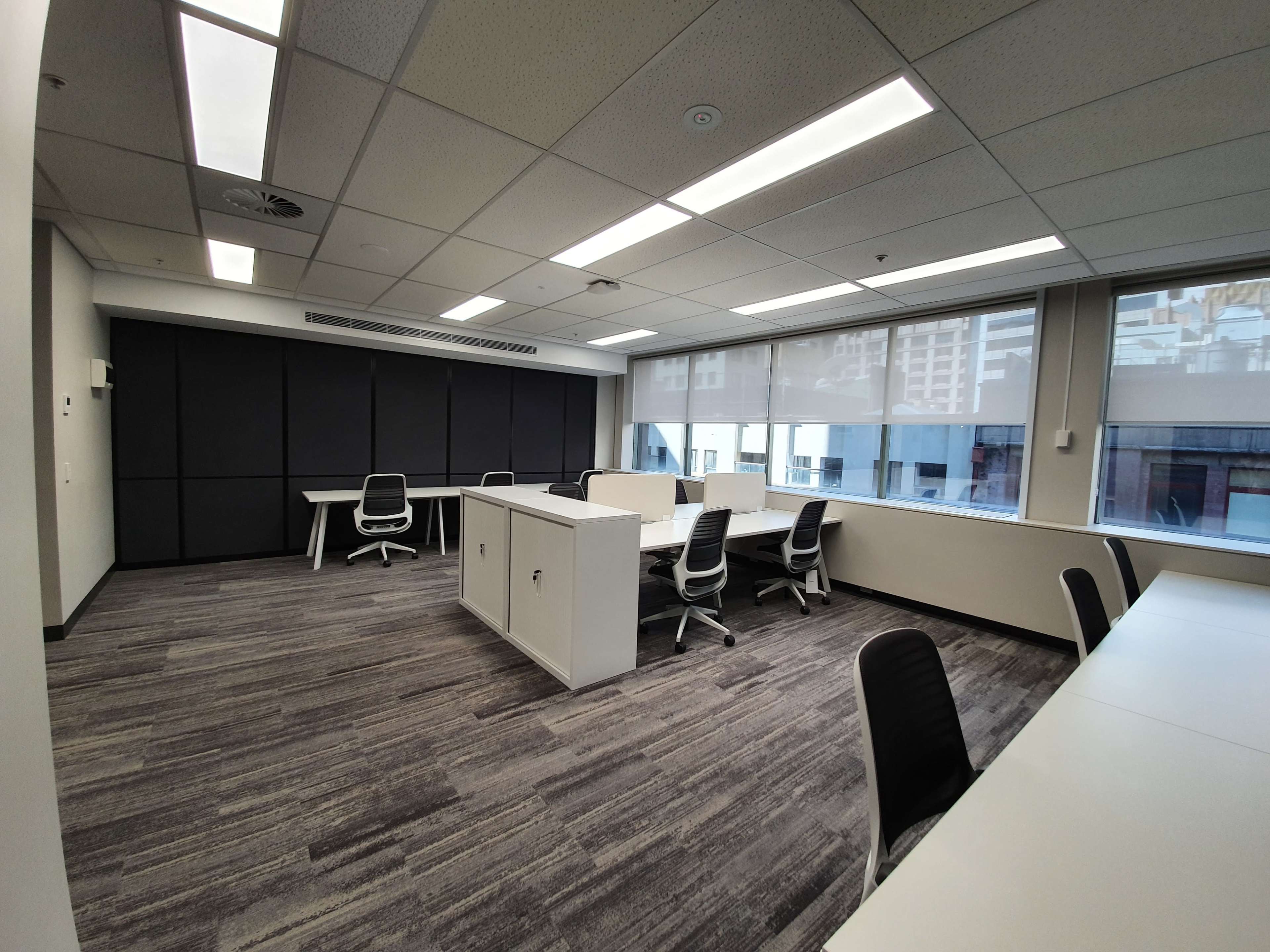 The image shows a modern office space with multiple workstations, large windows, and minimalistic furniture.