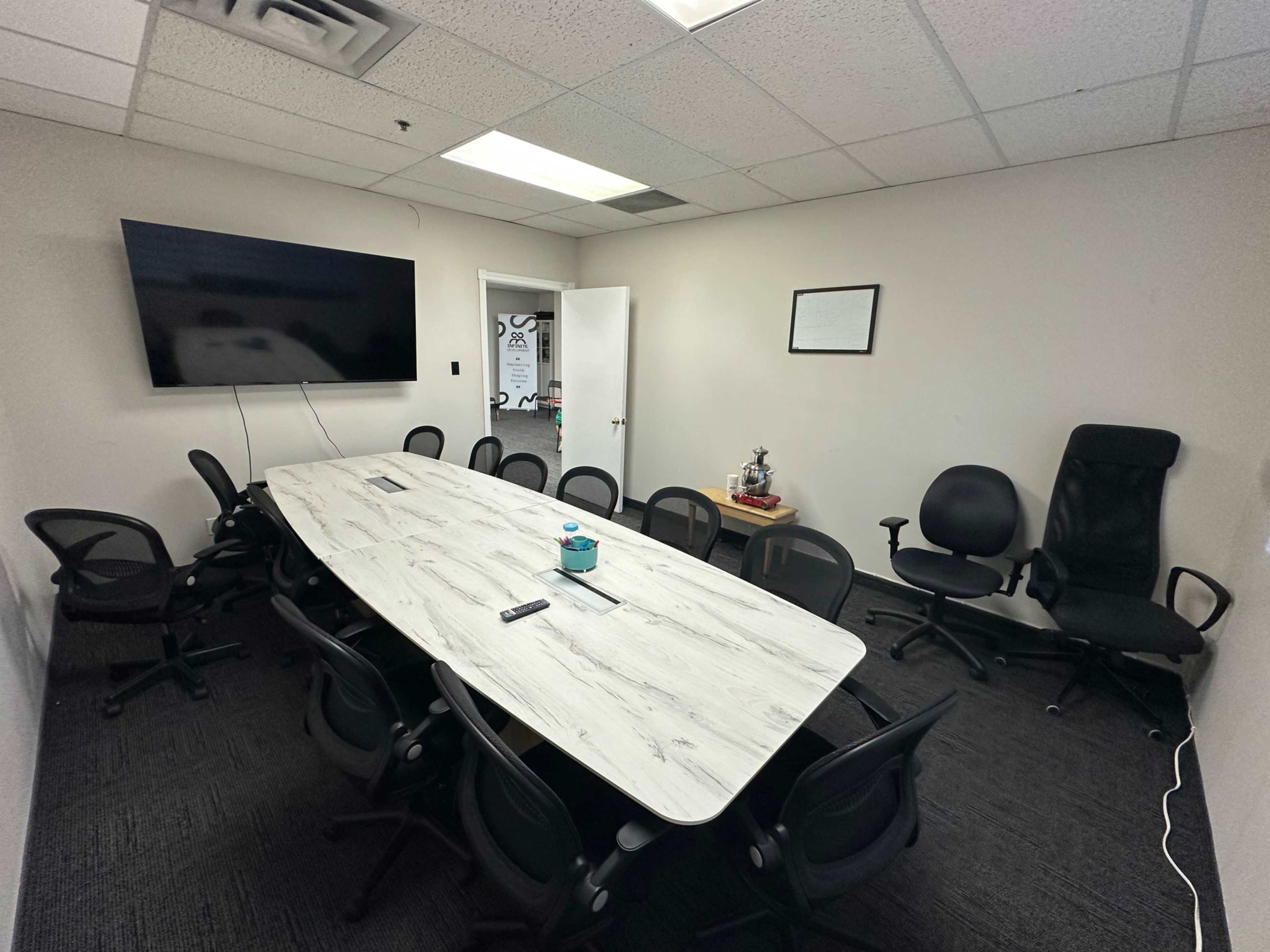 A conference room features a large table surrounded by multiple office chairs and a television mounted on the wall.
