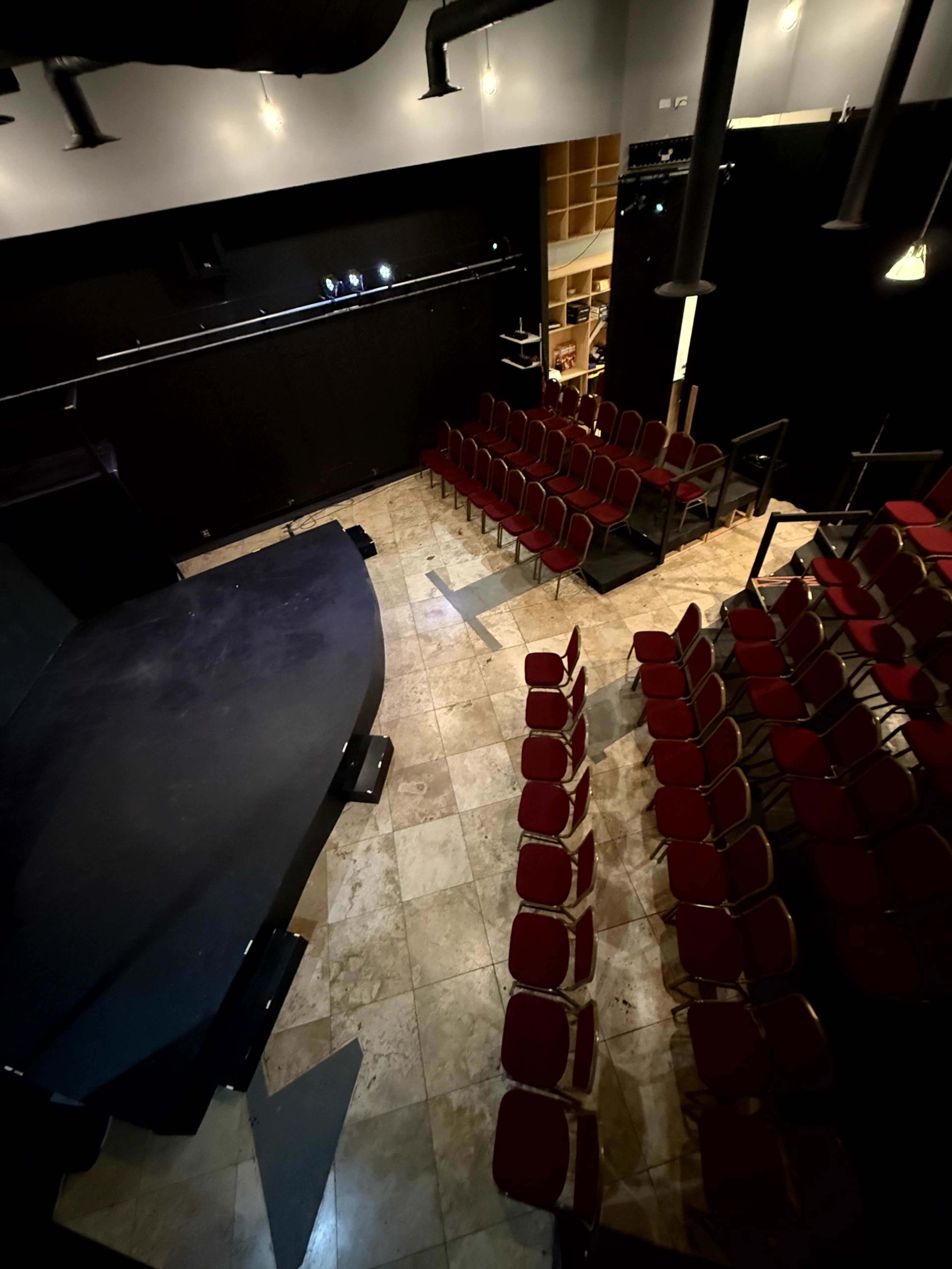 The image shows an empty theater with a dark stage and rows of red chairs facing it.