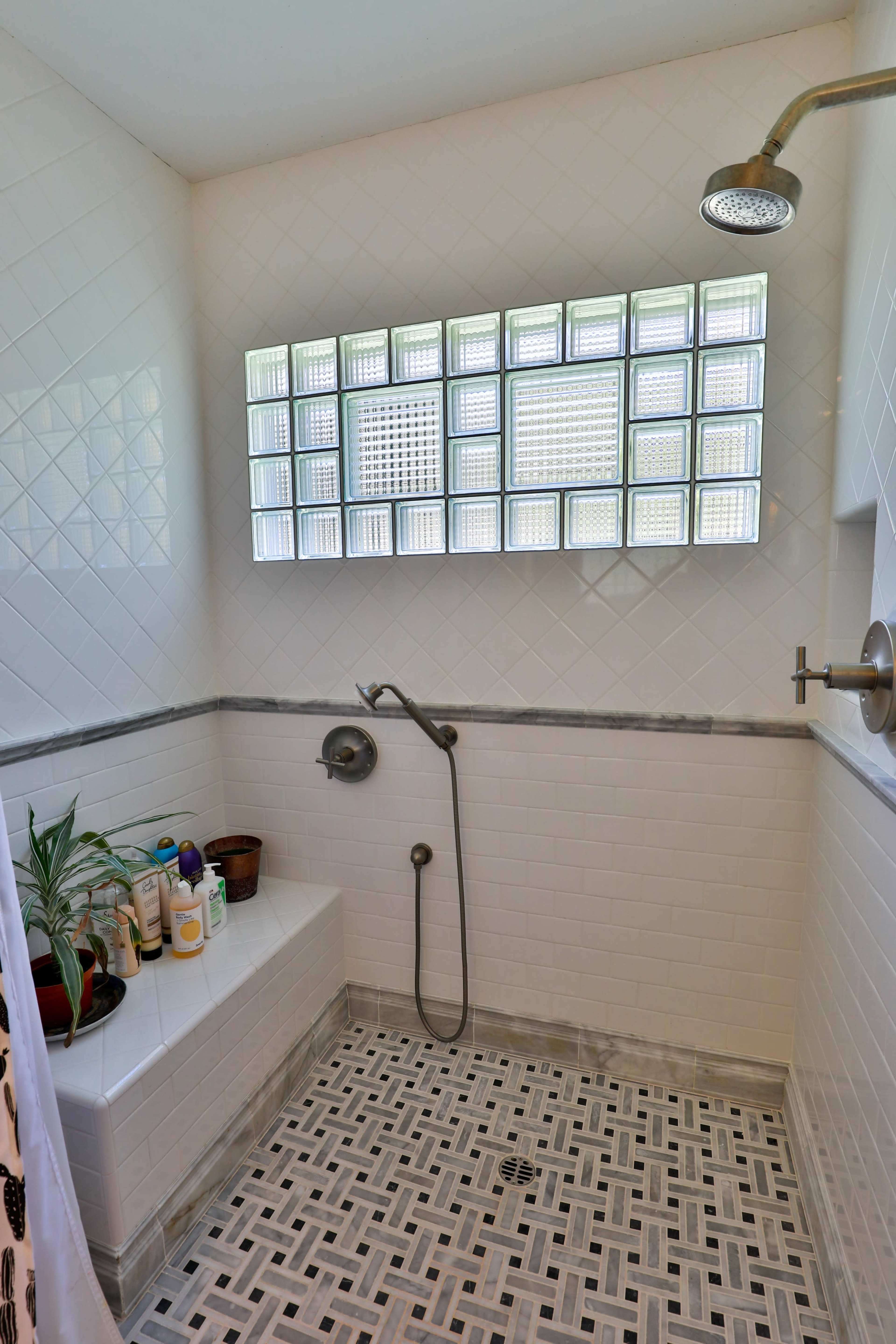 A modern shower with white tile walls, a glass block window, and a patterned tile floor.