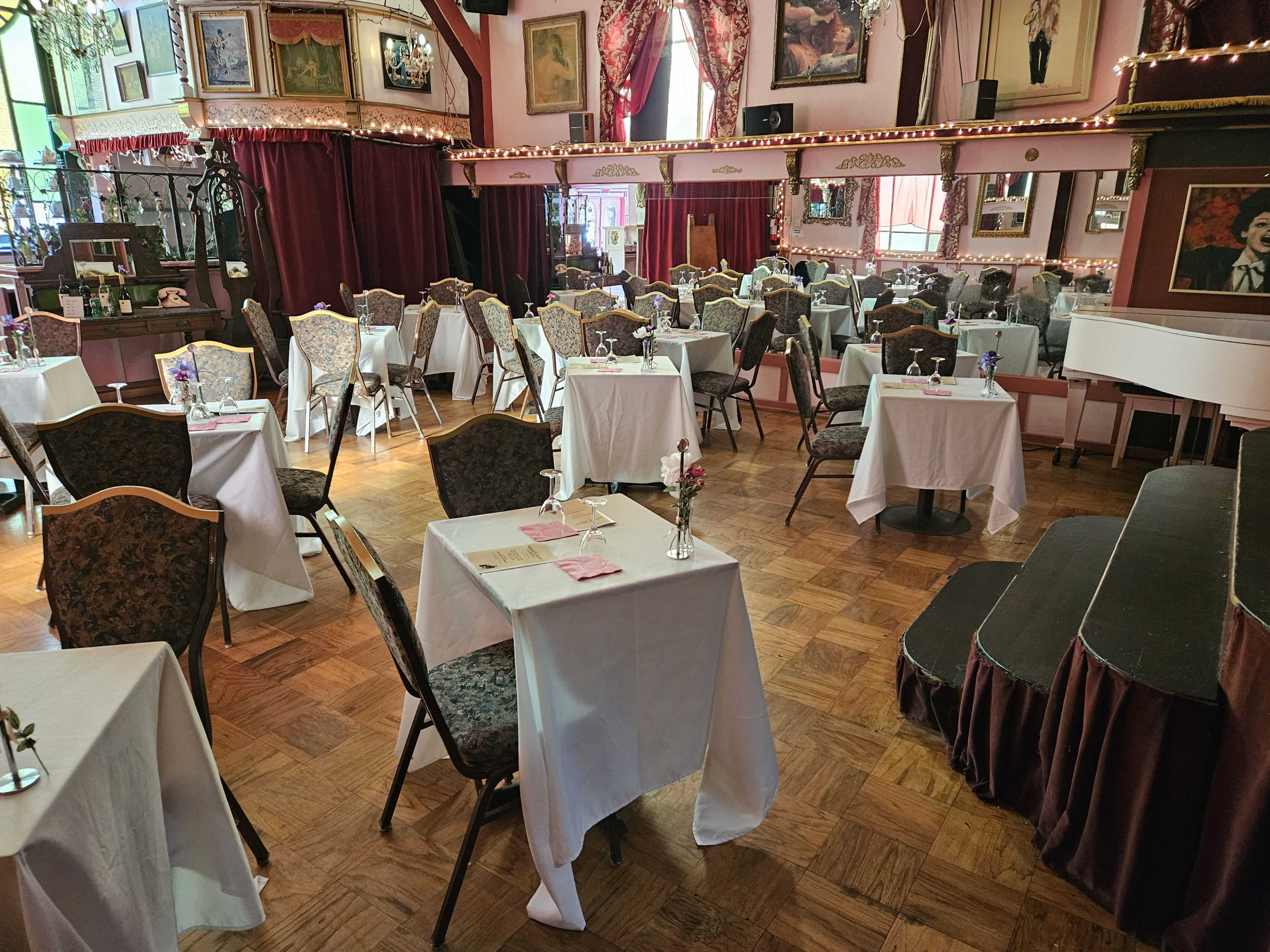 A dining area with neatly arranged tables covered in white tablecloths and surrounded by vintage decorations and framed artwork.