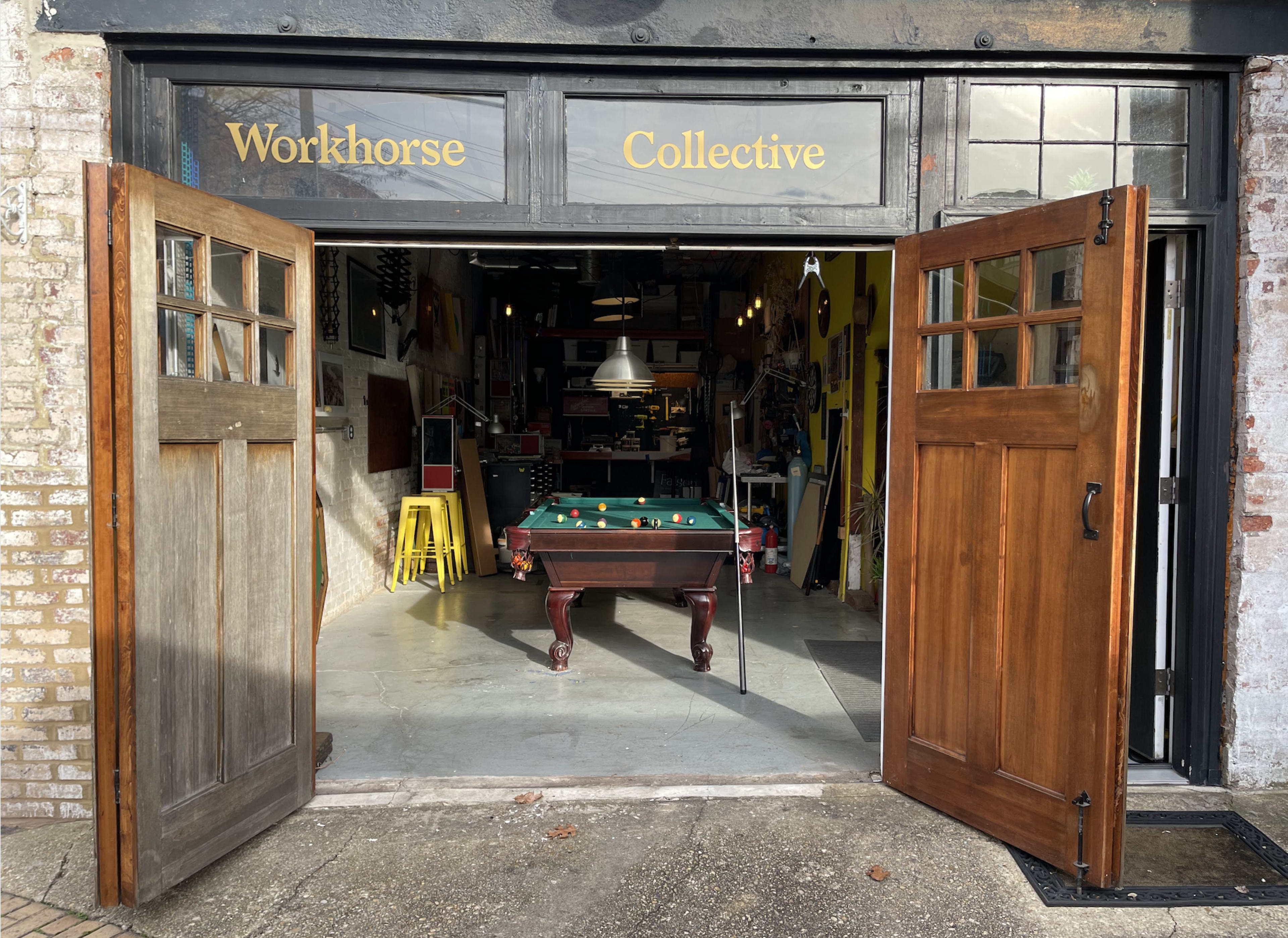 The entrance of a workshop named "Workhorse Collective" features an open double door leading to an interior with a green pool table and various tools and equipment visible inside.