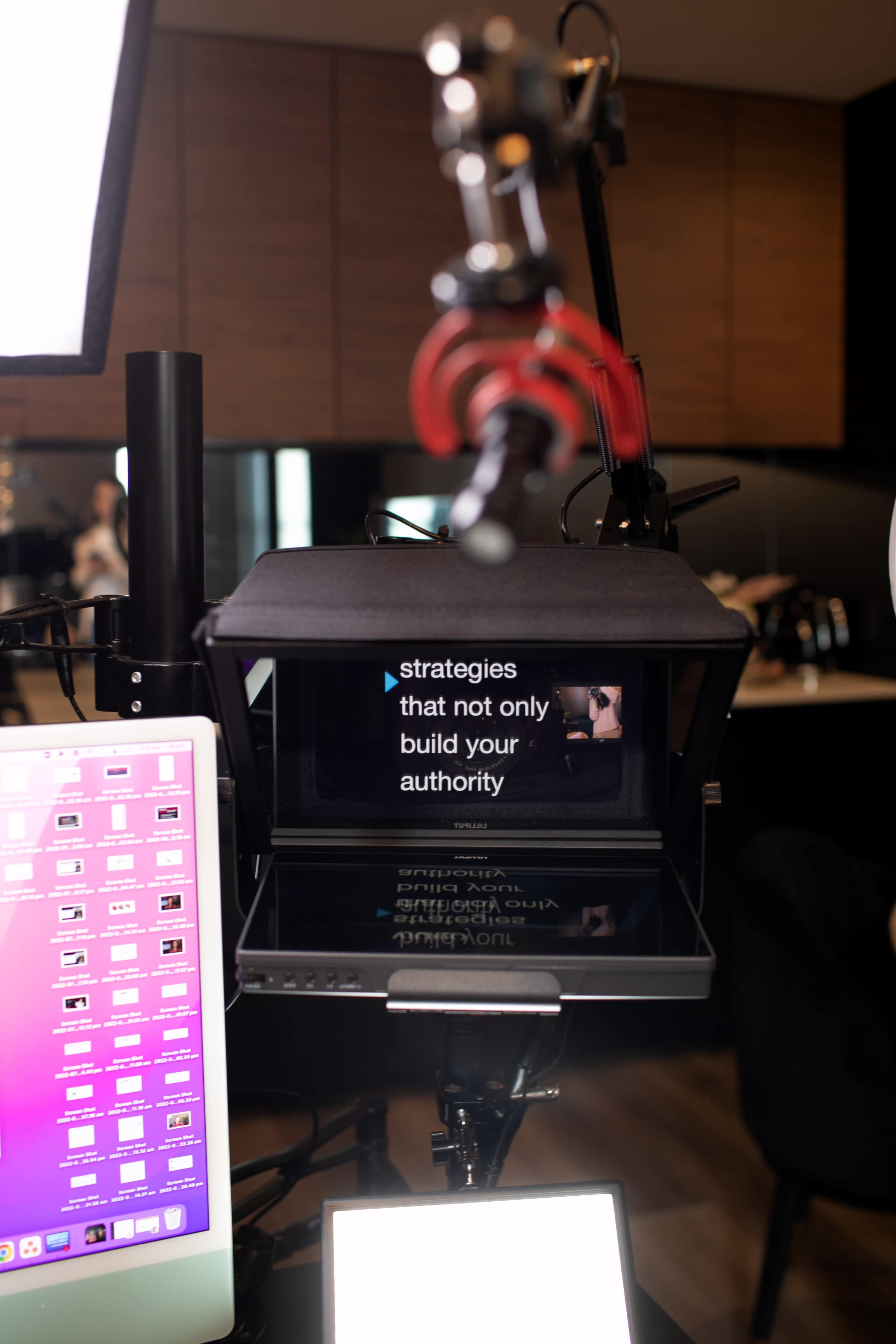 A teleprompter displays text about strategies for building authority, positioned in a modern filming setup with a computer nearby.