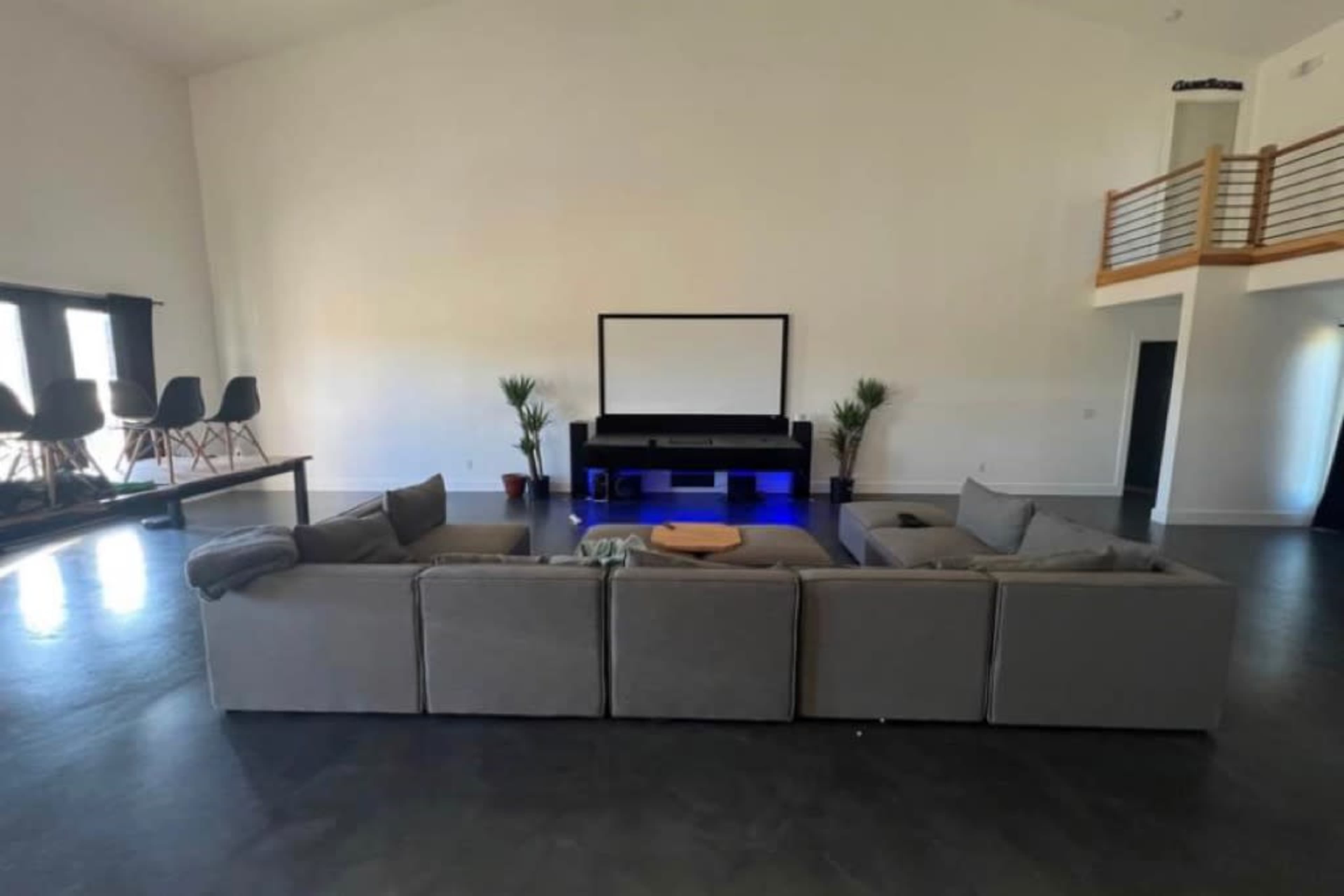 A spacious living room features a large sectional sofa facing a home theater setup with a screen and entertainment unit, along with a few indoor plants.