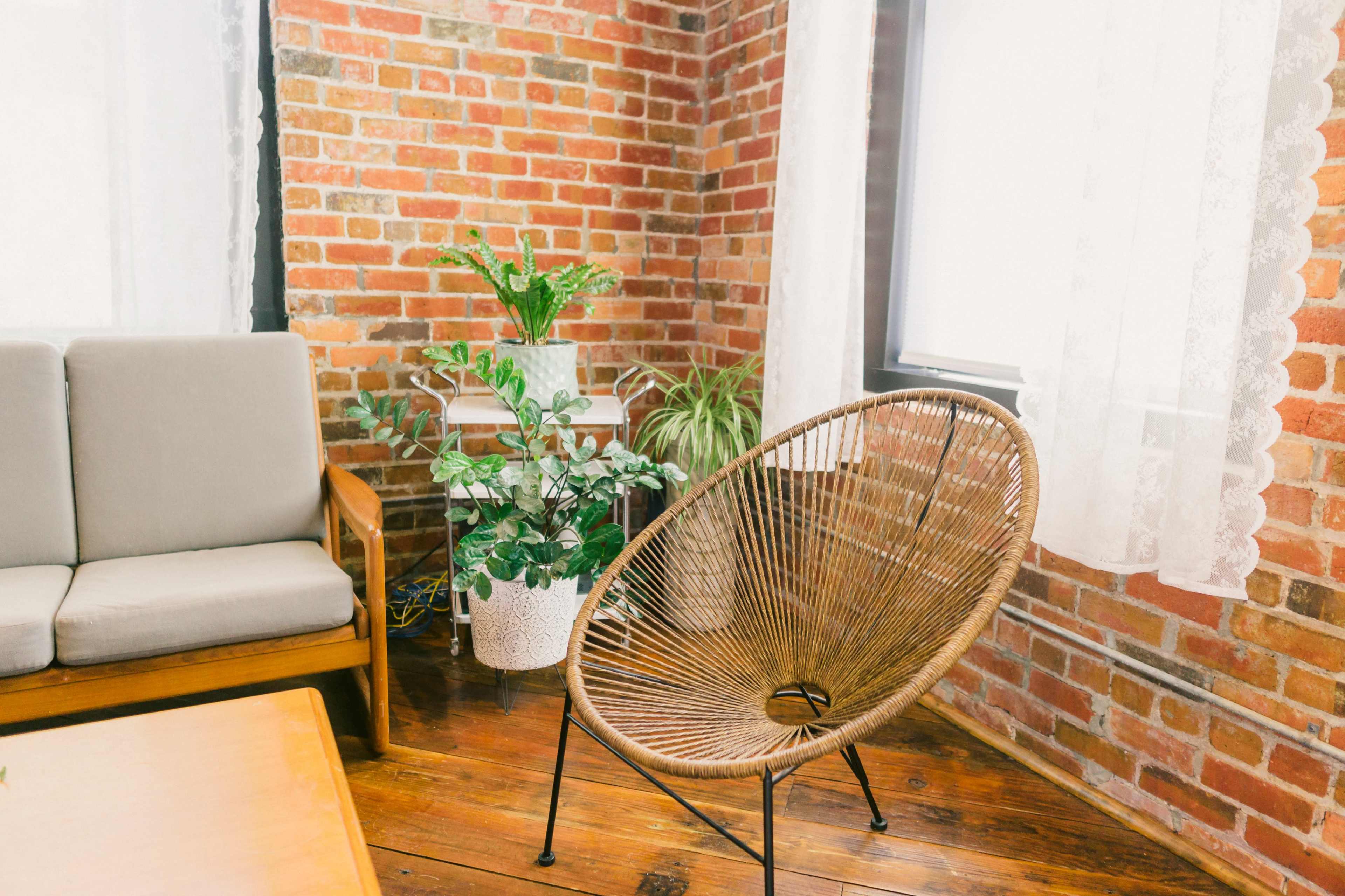A cozy sitting area with a wicker chair, a small table, and several potted plants against a backdrop of exposed brick walls.