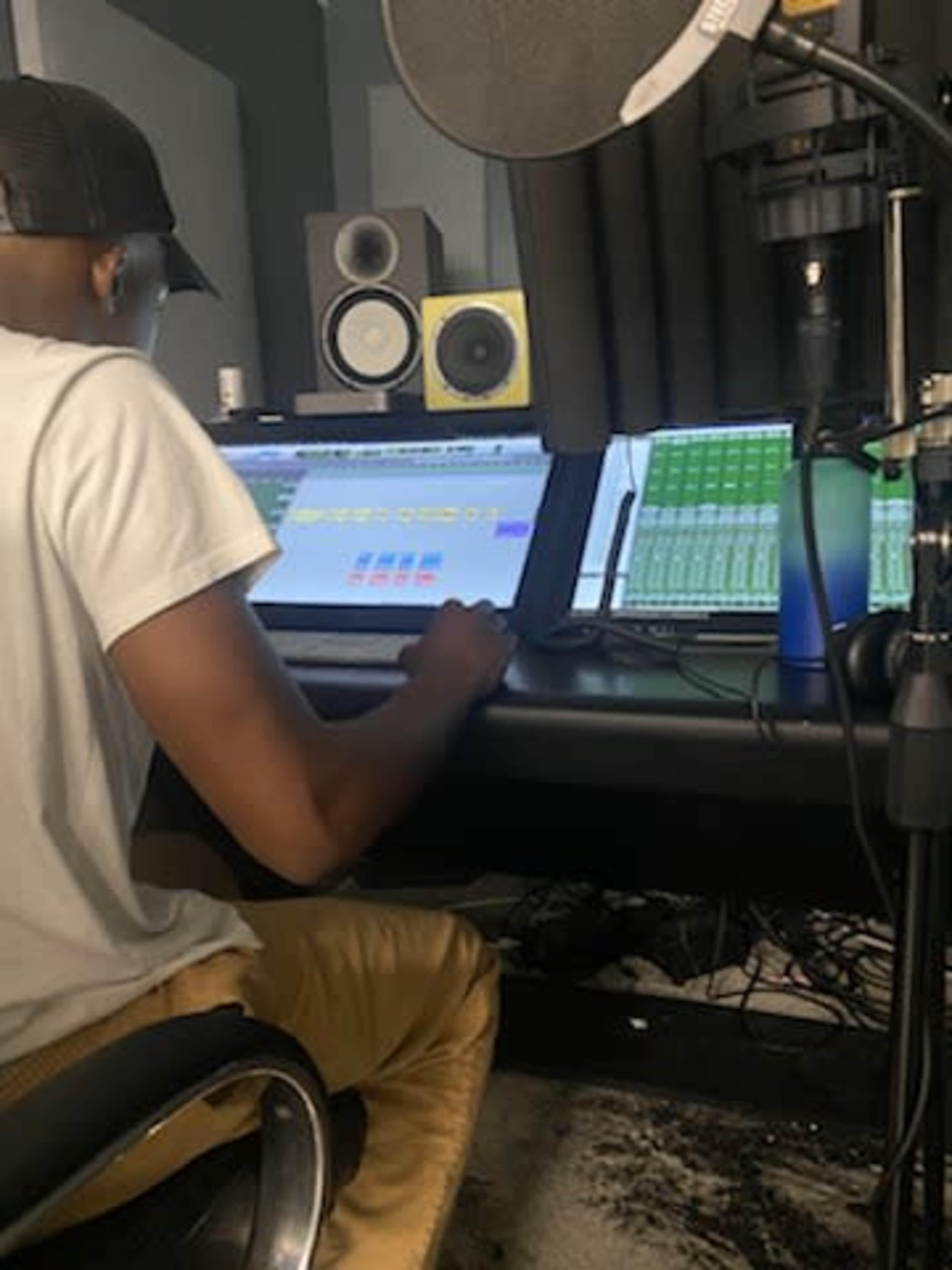 A person is sitting at a music production workstation, adjusting audio levels on a computer screen in a recording studio.