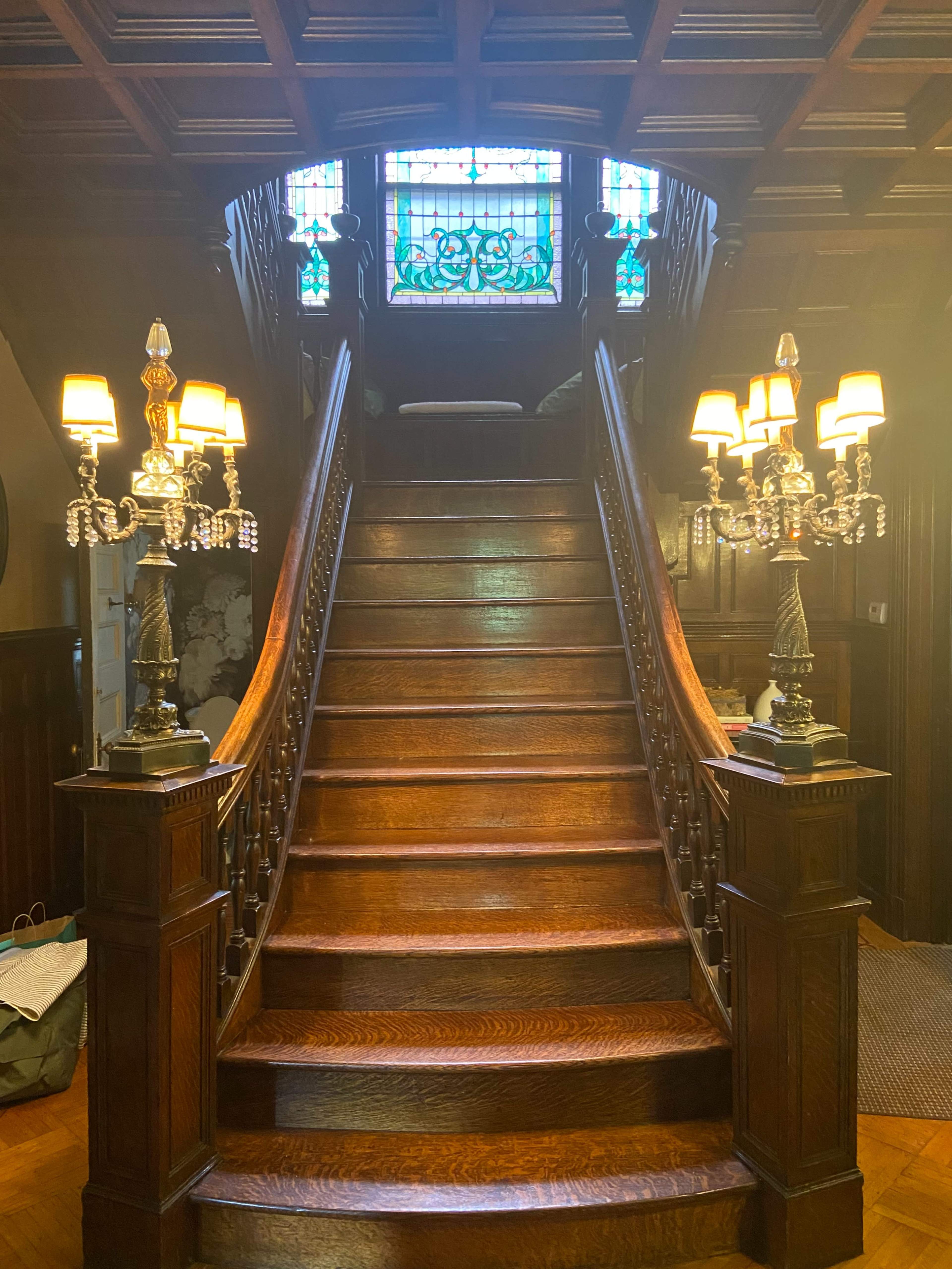 A grand wooden staircase with an ornate balustrade leading up to a stained glass window.