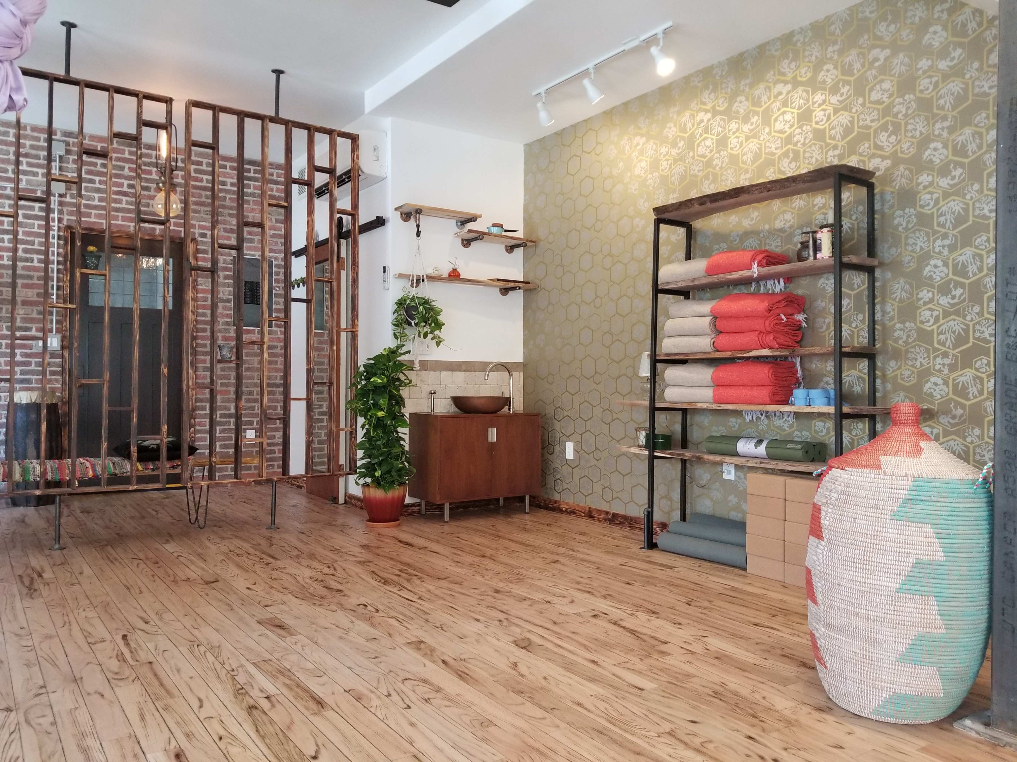 A spacious indoor area featuring wooden flooring, a decorative green wall, shelves with rolled towels, a potted plant, and a woven basket.