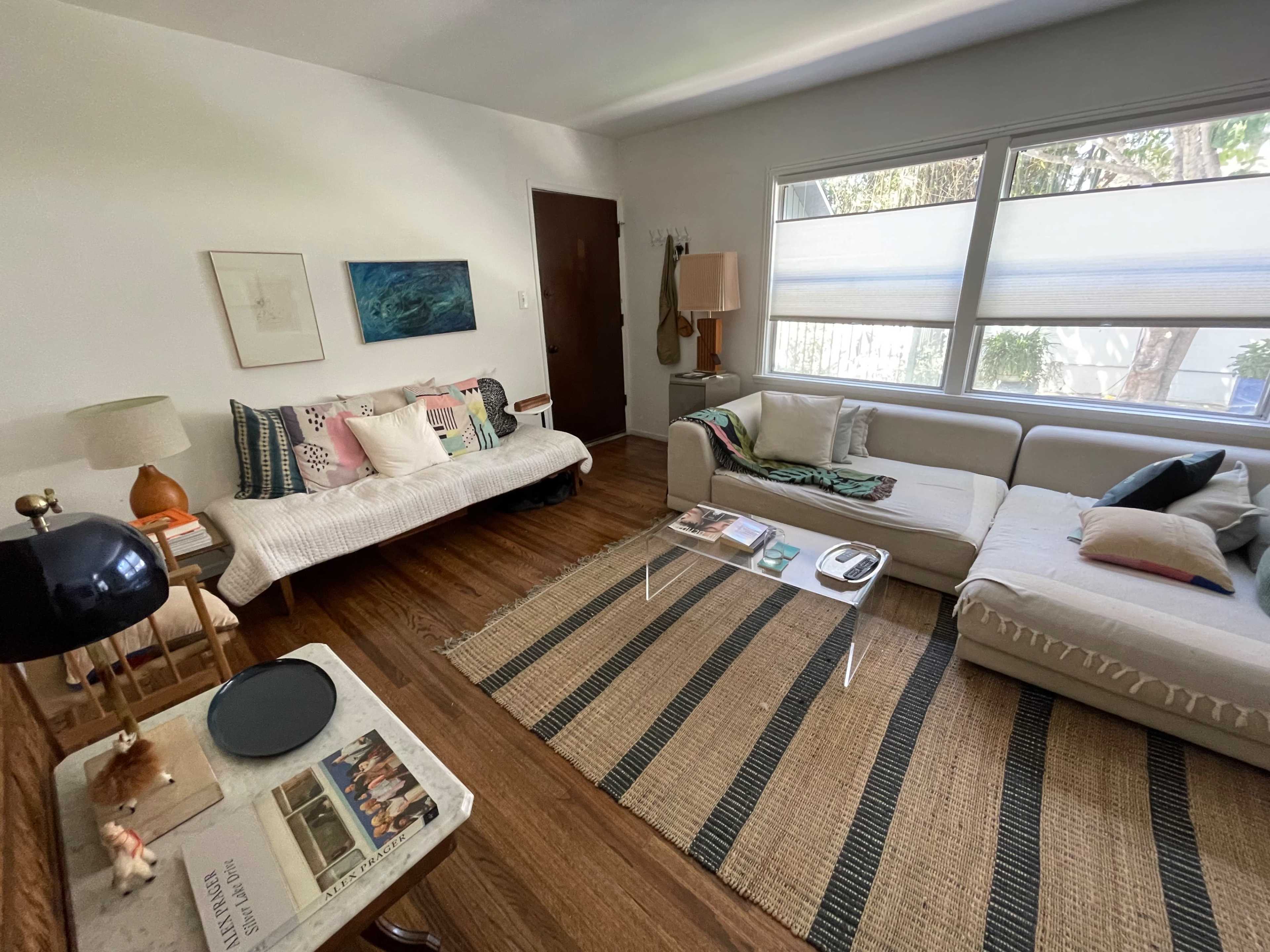 The image shows a bright living room with a light-colored sofa, a white daybed, and a patterned area rug on a wooden floor.
