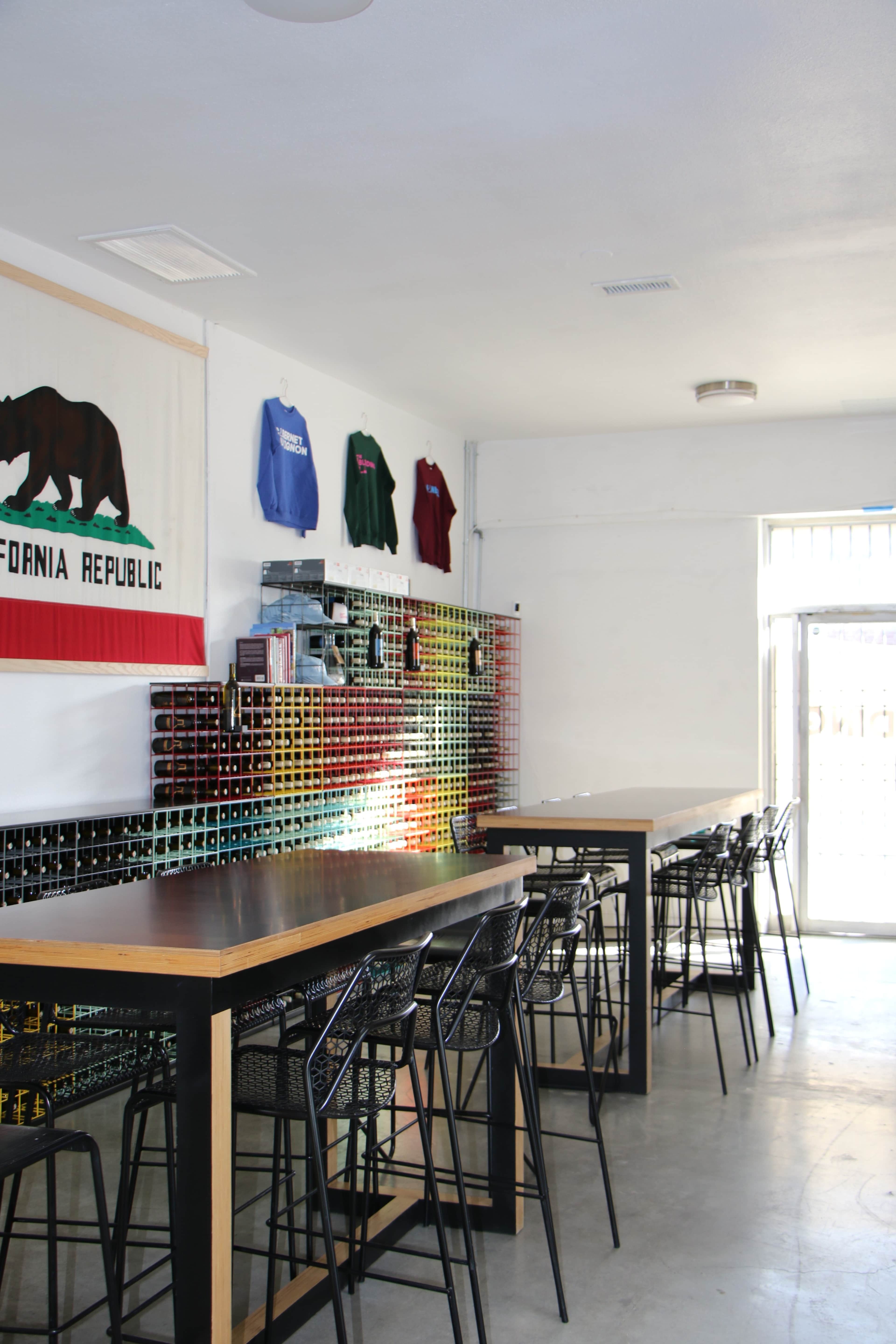 The image shows a modern bar area with high tables and chairs, a display of colorful cans on the wall, and California Republic merchandise hanging above.