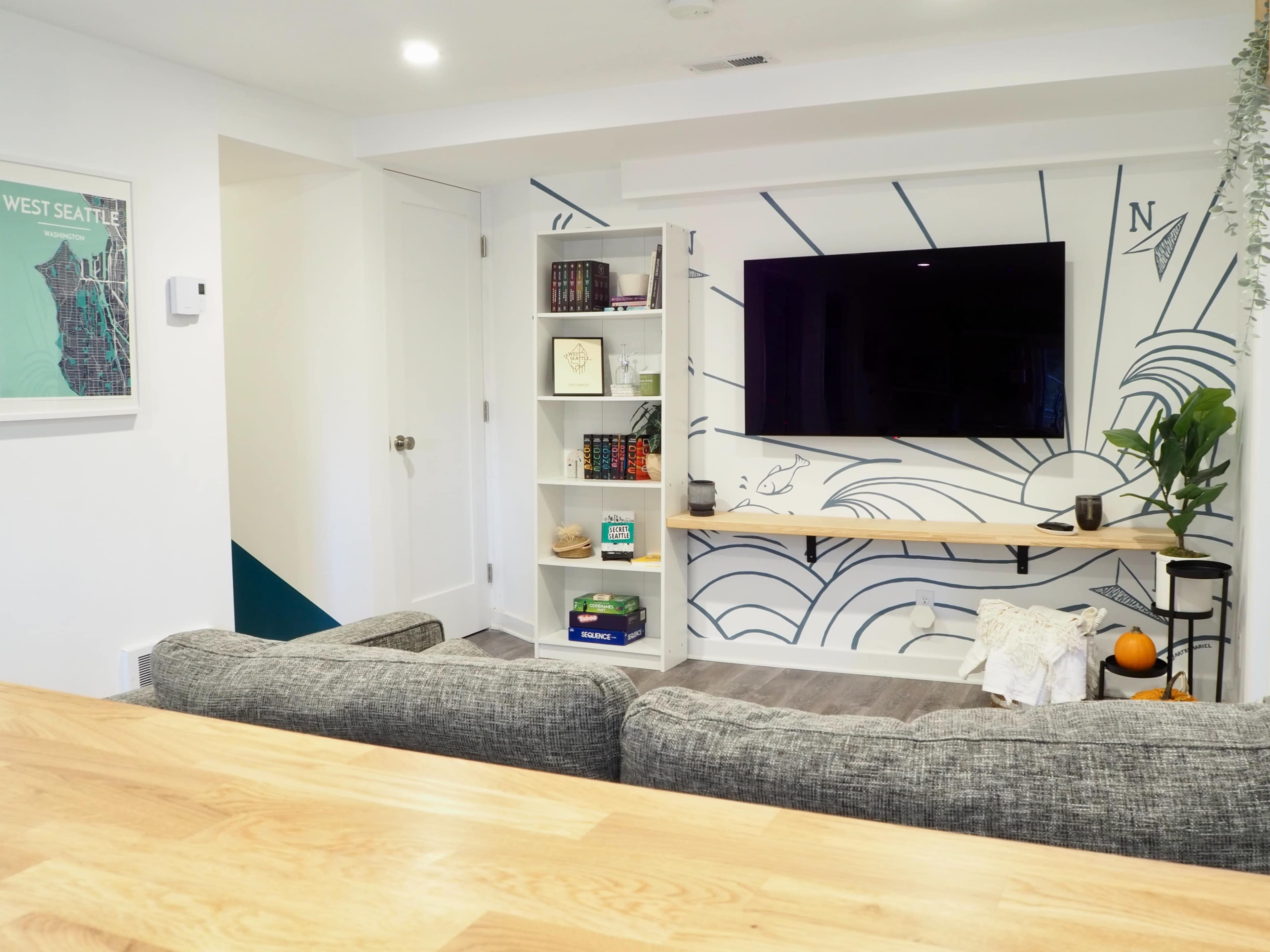 A modern living room with a large wall-mounted television, a bookshelf filled with books, and a decorative wall featuring a sun graphic.