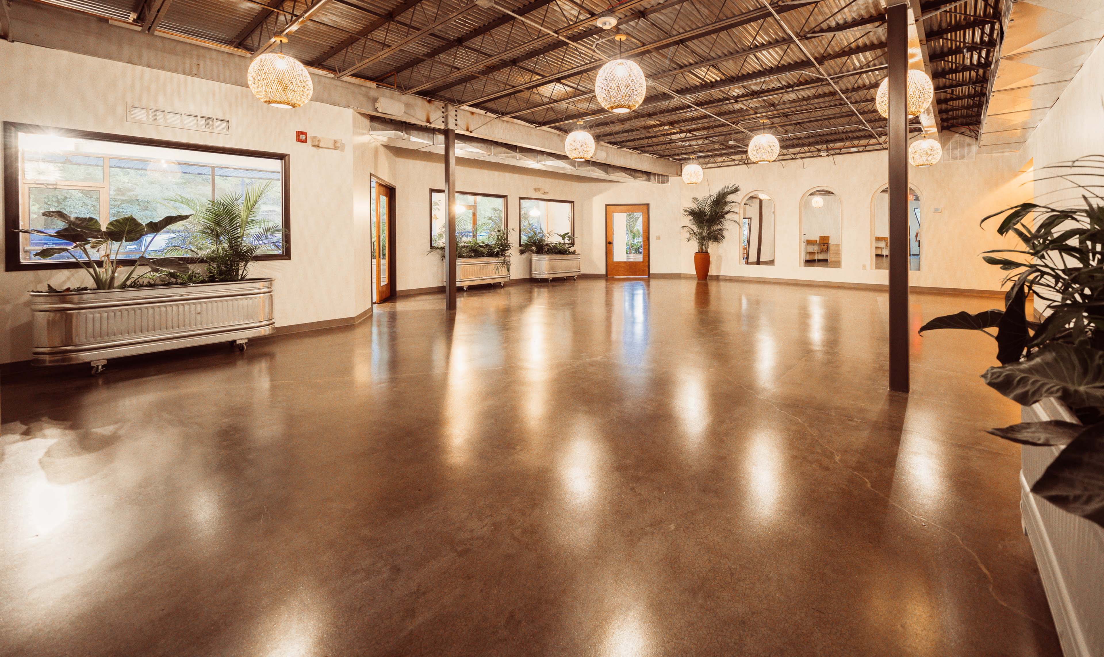 The image shows a spacious, well-lit indoor area featuring polished concrete floors, large windows, and decorative hanging light fixtures.