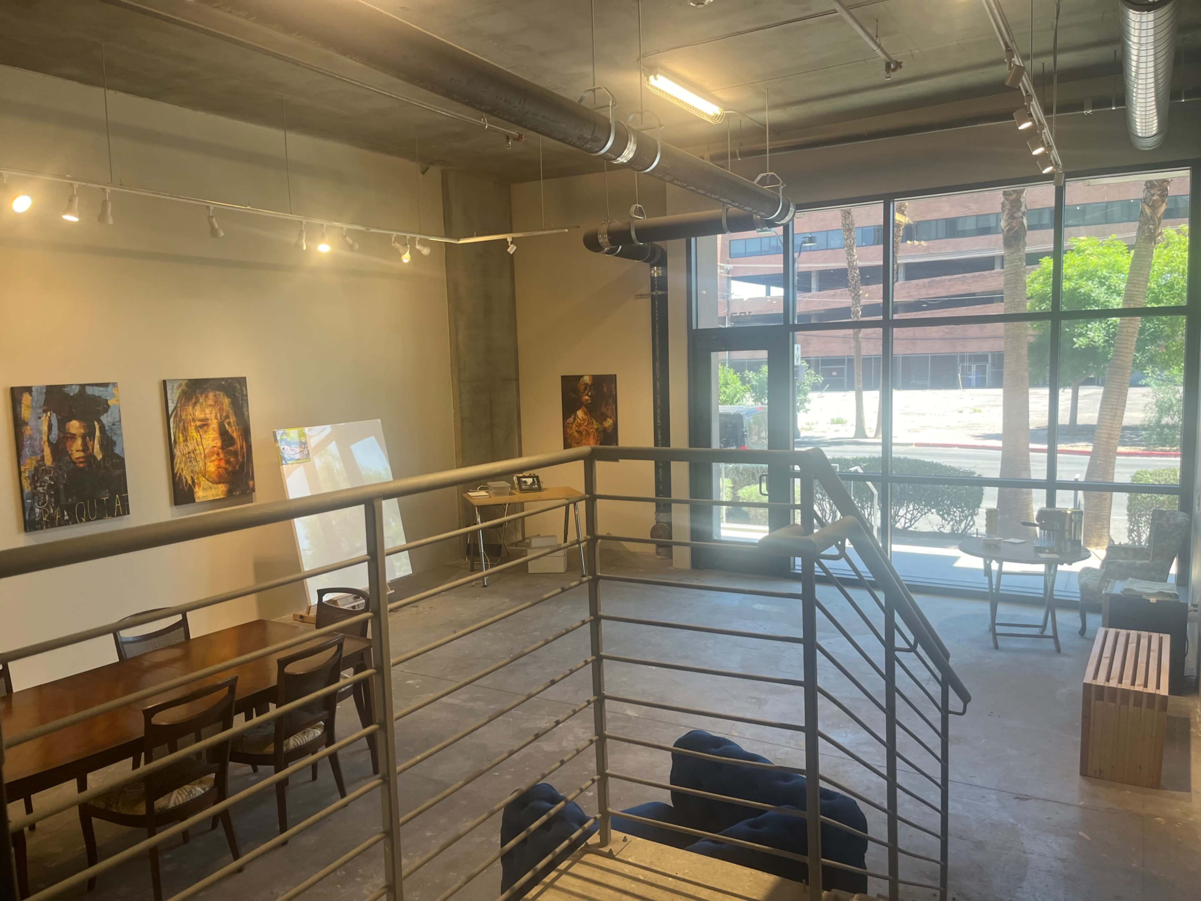 A spacious art gallery with paintings on the walls, a long table, and large windows letting in natural light.