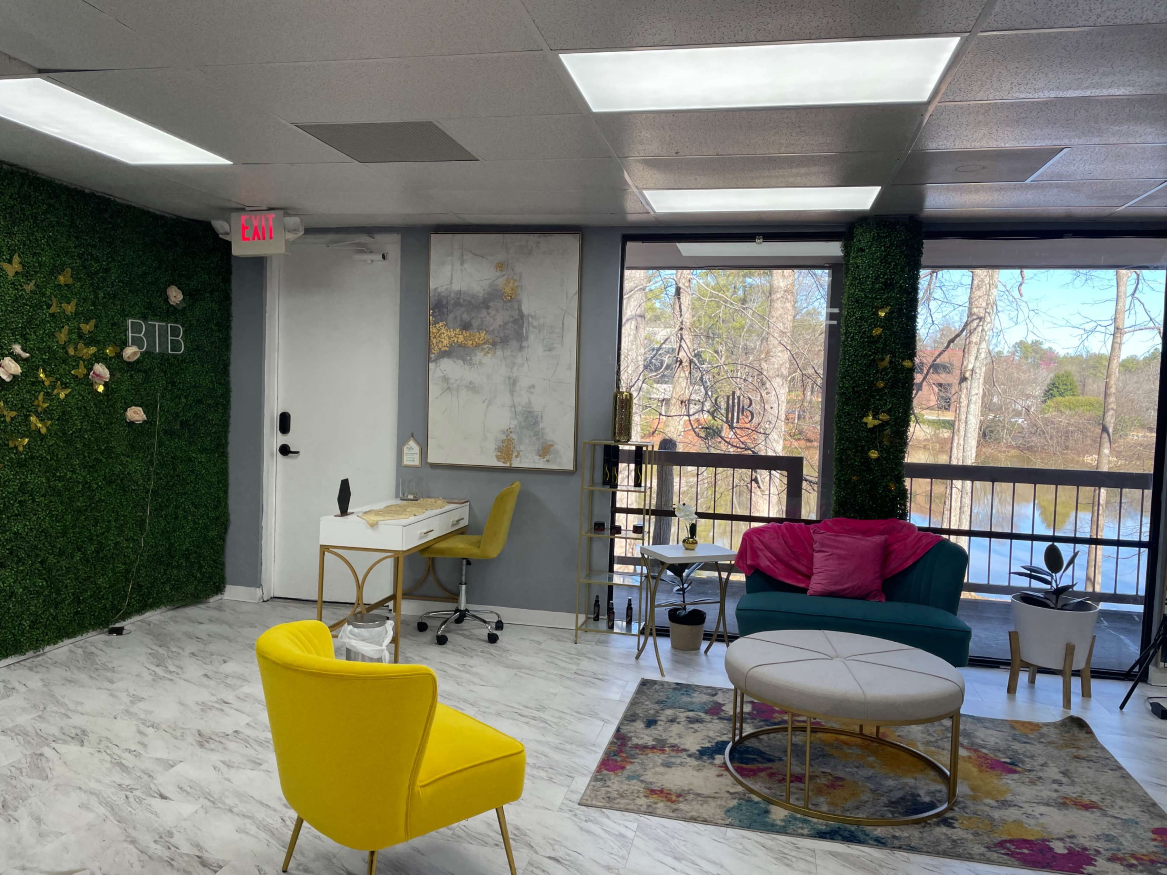 A modern interior space with green wall accents, a seating area featuring a yellow chair, and large windows overlooking a body of water.