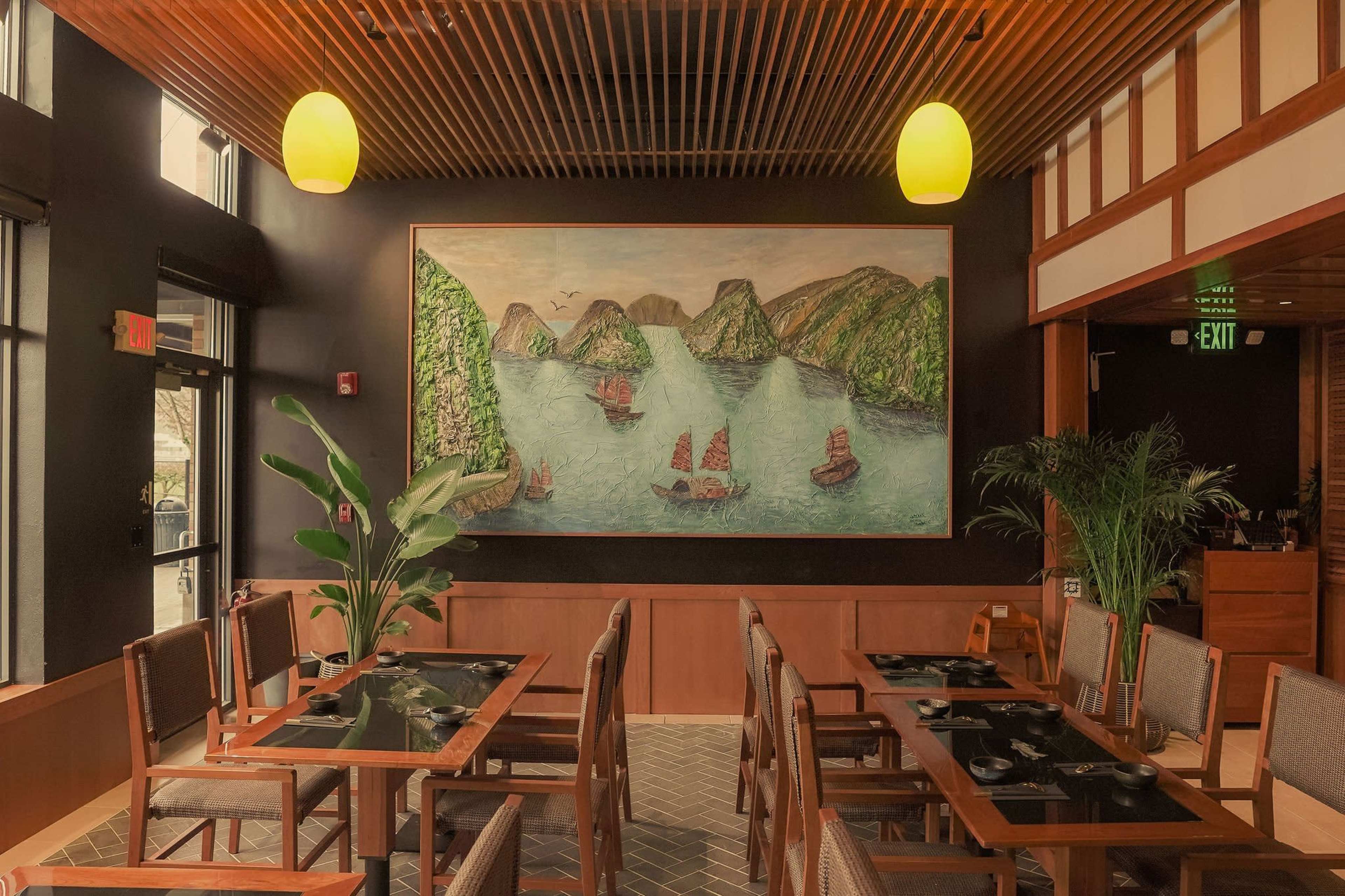 The interior of a restaurant features wooden tables, chairs, and a large mural depicting a coastal scene with boats on water.