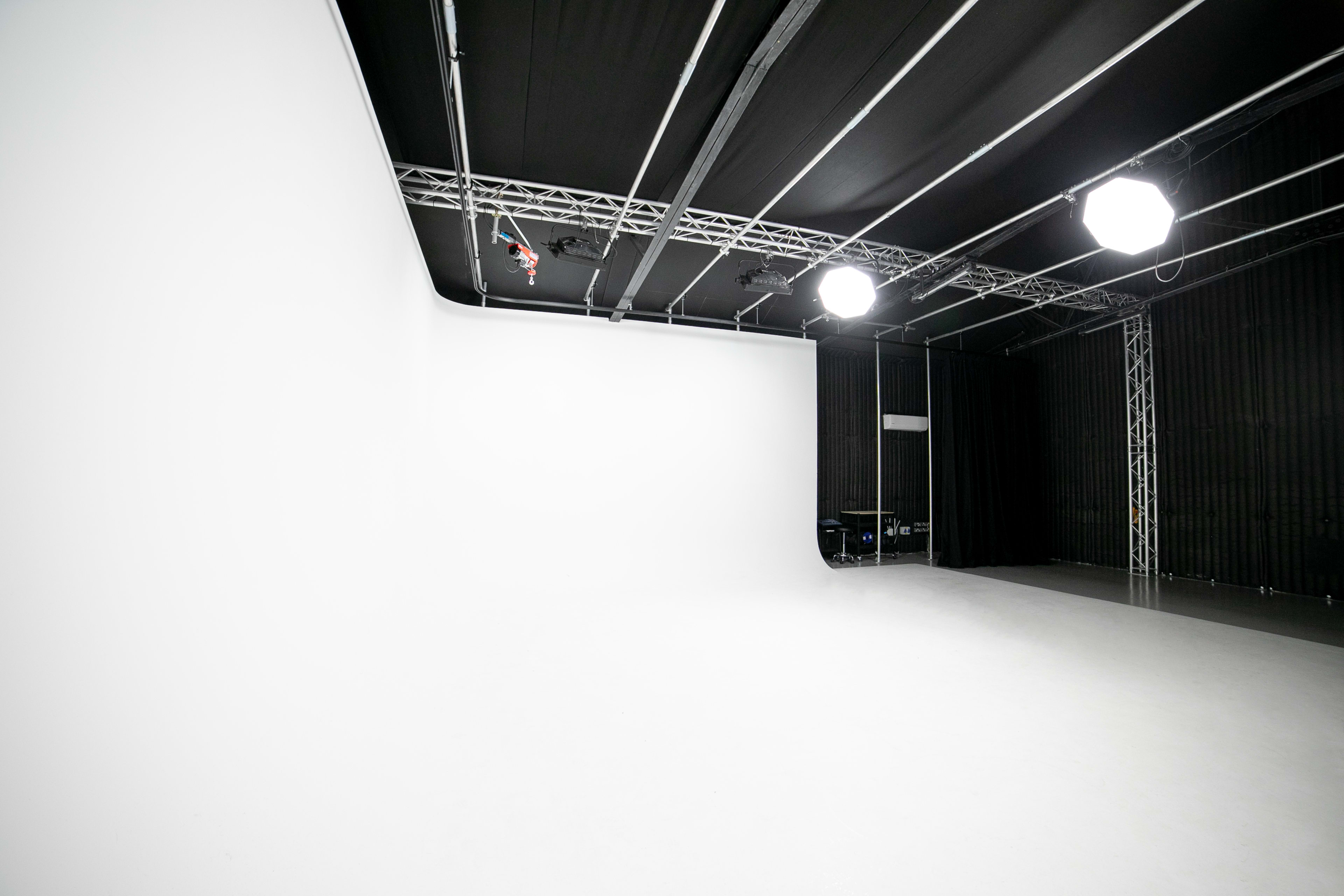 The image shows a spacious photography studio with a blank white backdrop and overhead lighting fixtures.