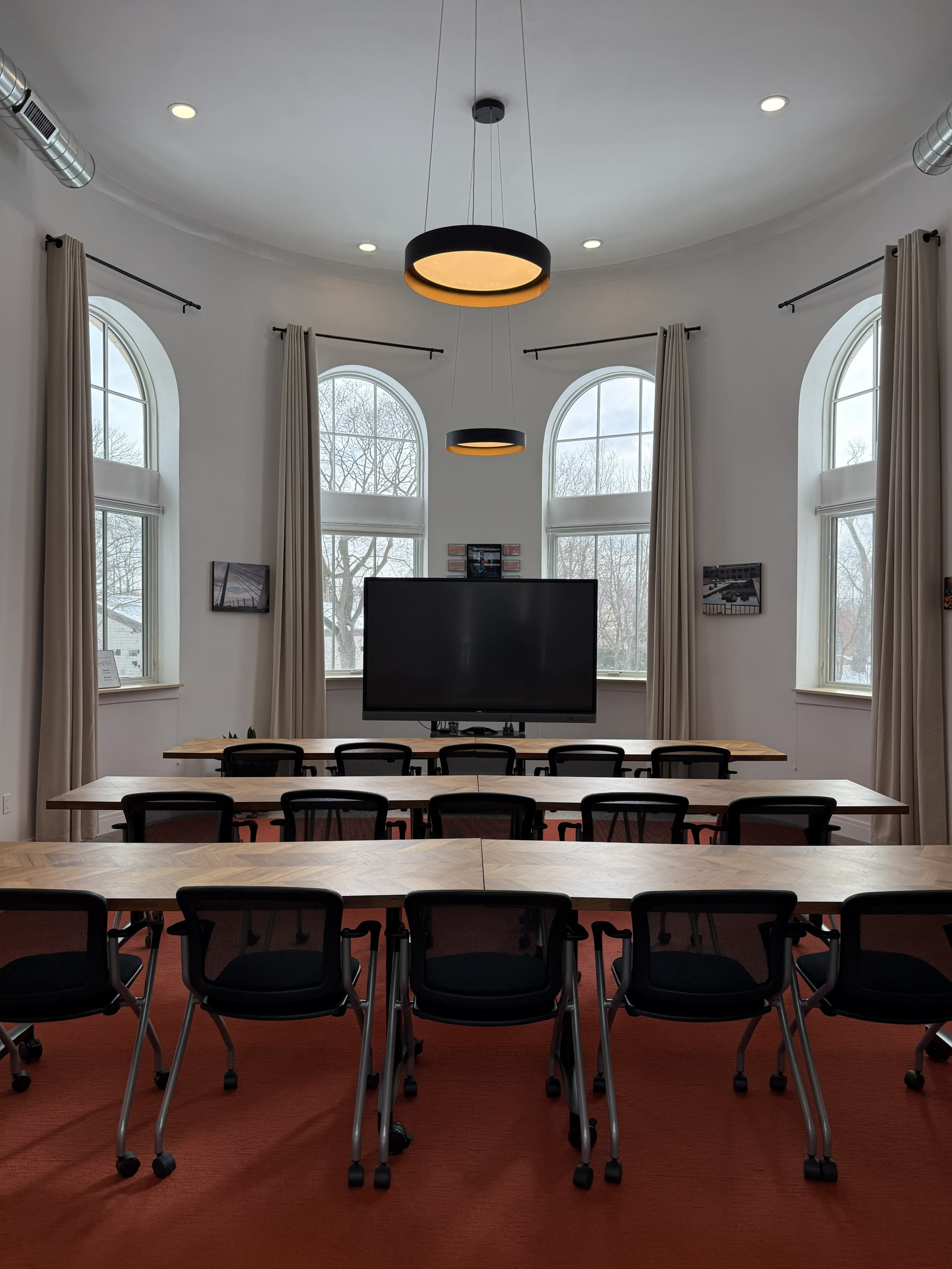 The image shows a conference room with multiple tables arranged in a U-shape, chairs in front of each table, and large windows on the walls.