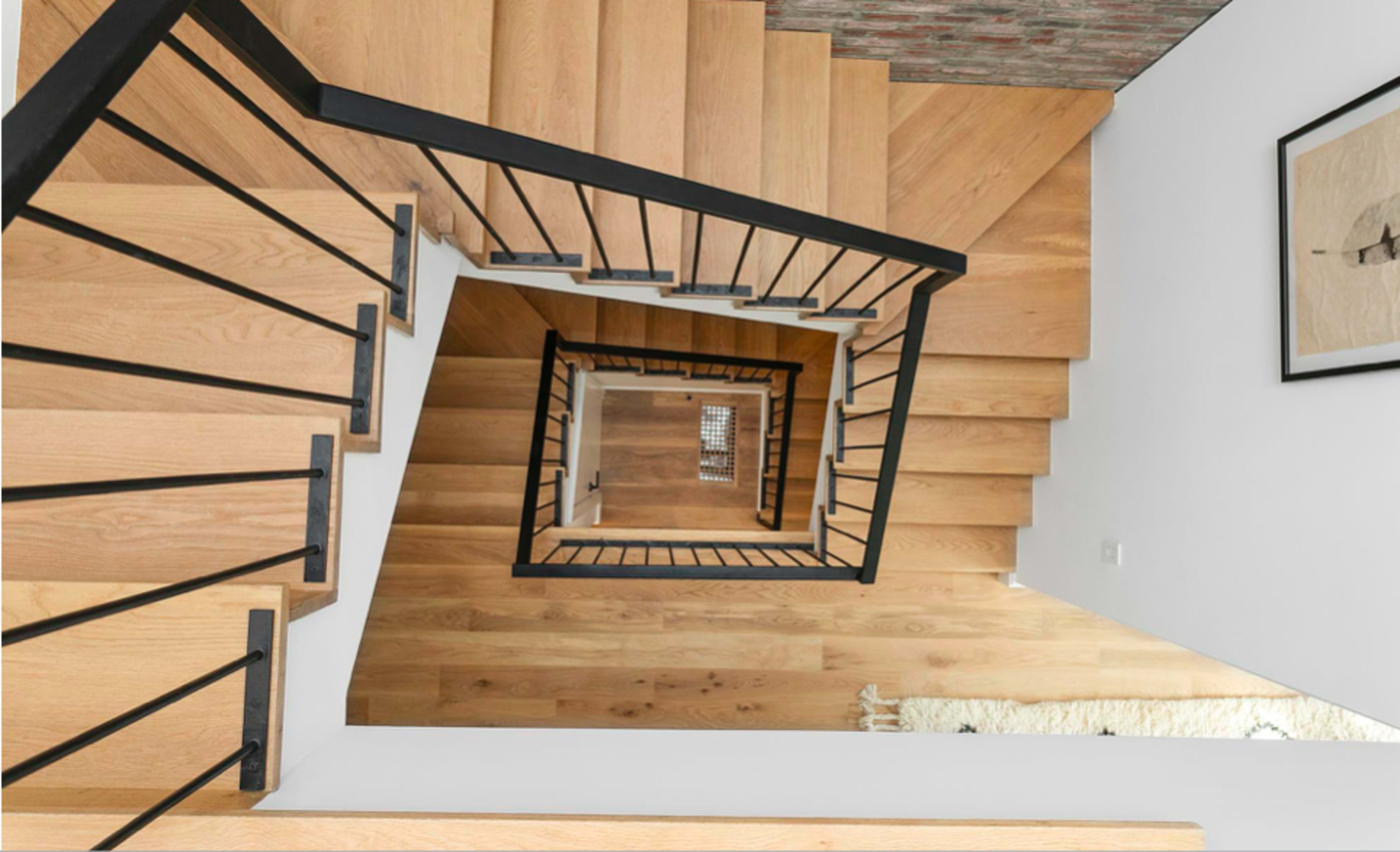 A wooden staircase spirals down with black metal railings, viewed from above.
