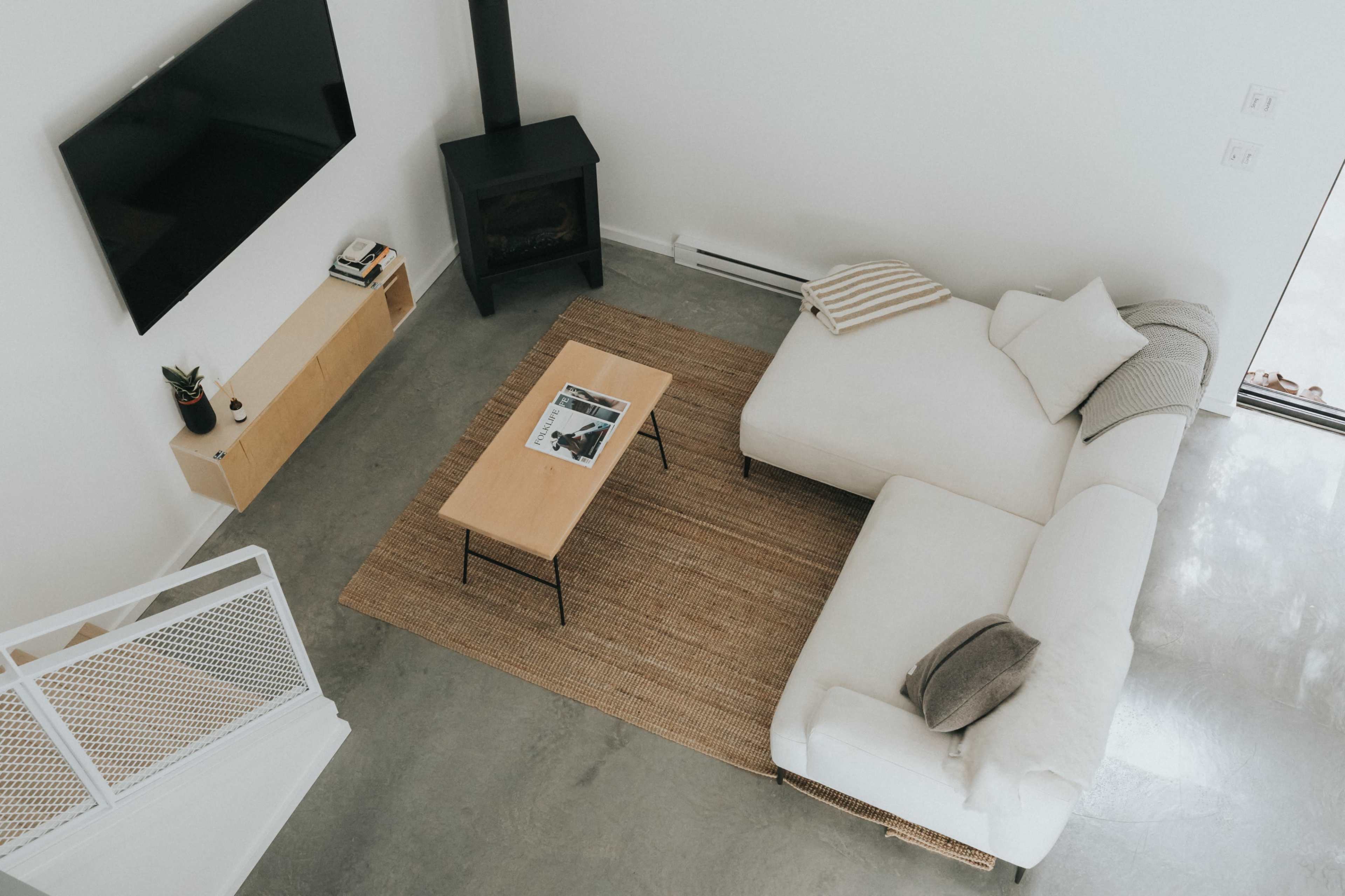 A stylish living room featuring a white sectional sofa, a wooden coffee table on a woven rug, and a mounted flat-screen TV.