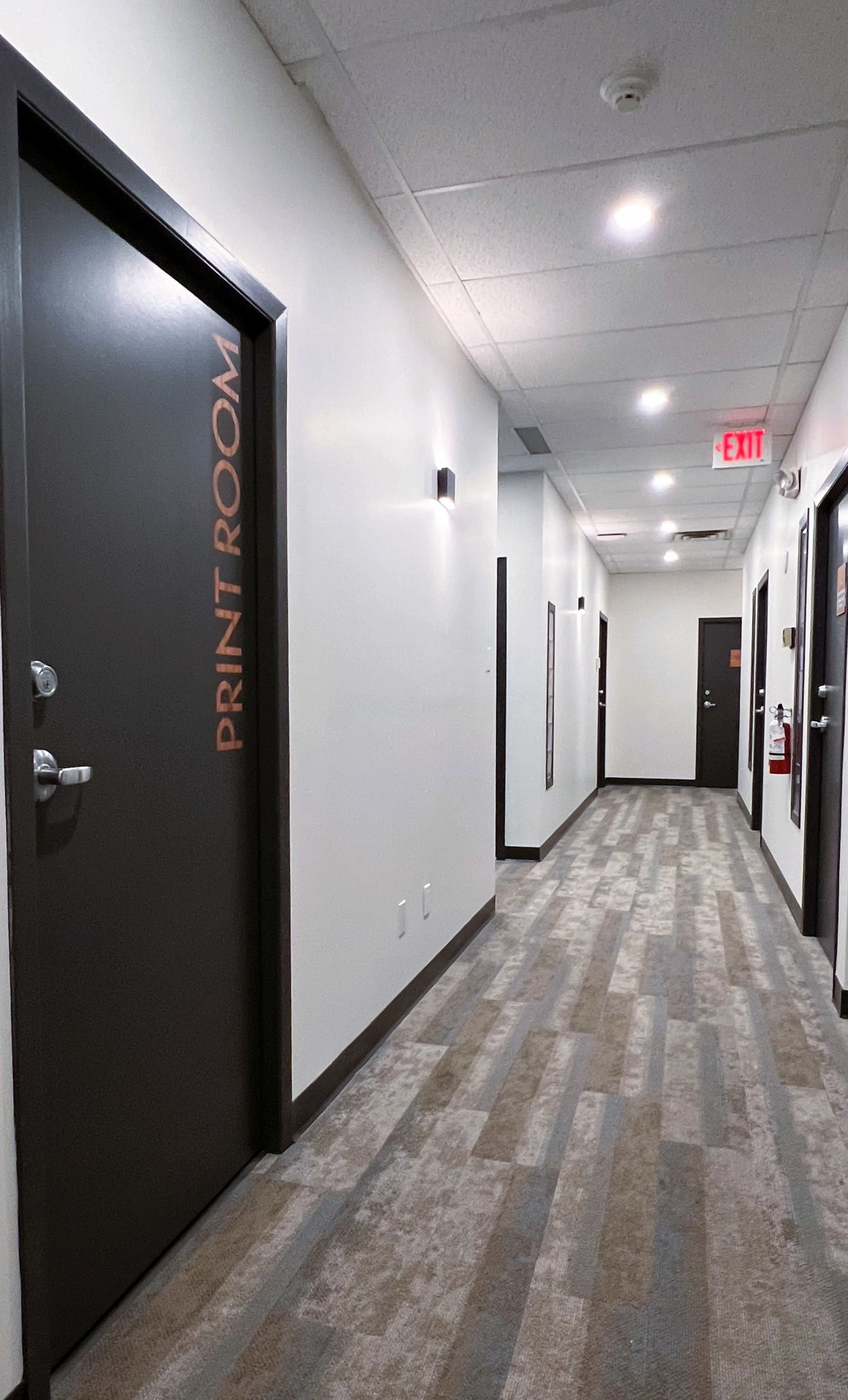 The image shows a well-lit hallway in a building, featuring doors on either side, with one door labeled "PRINT ROOM."