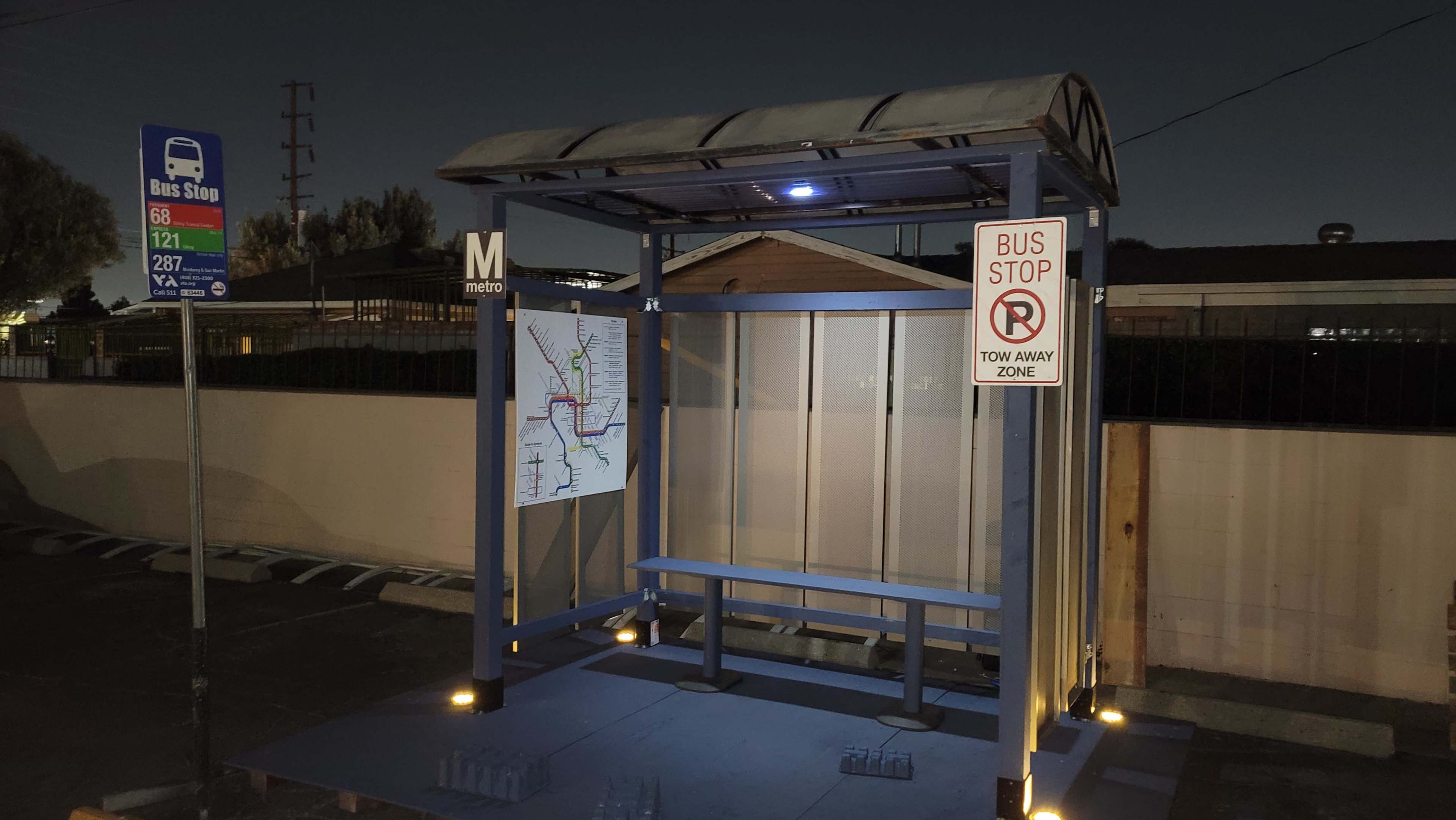 A bus stop shelter with a map and signage is illuminated at night.