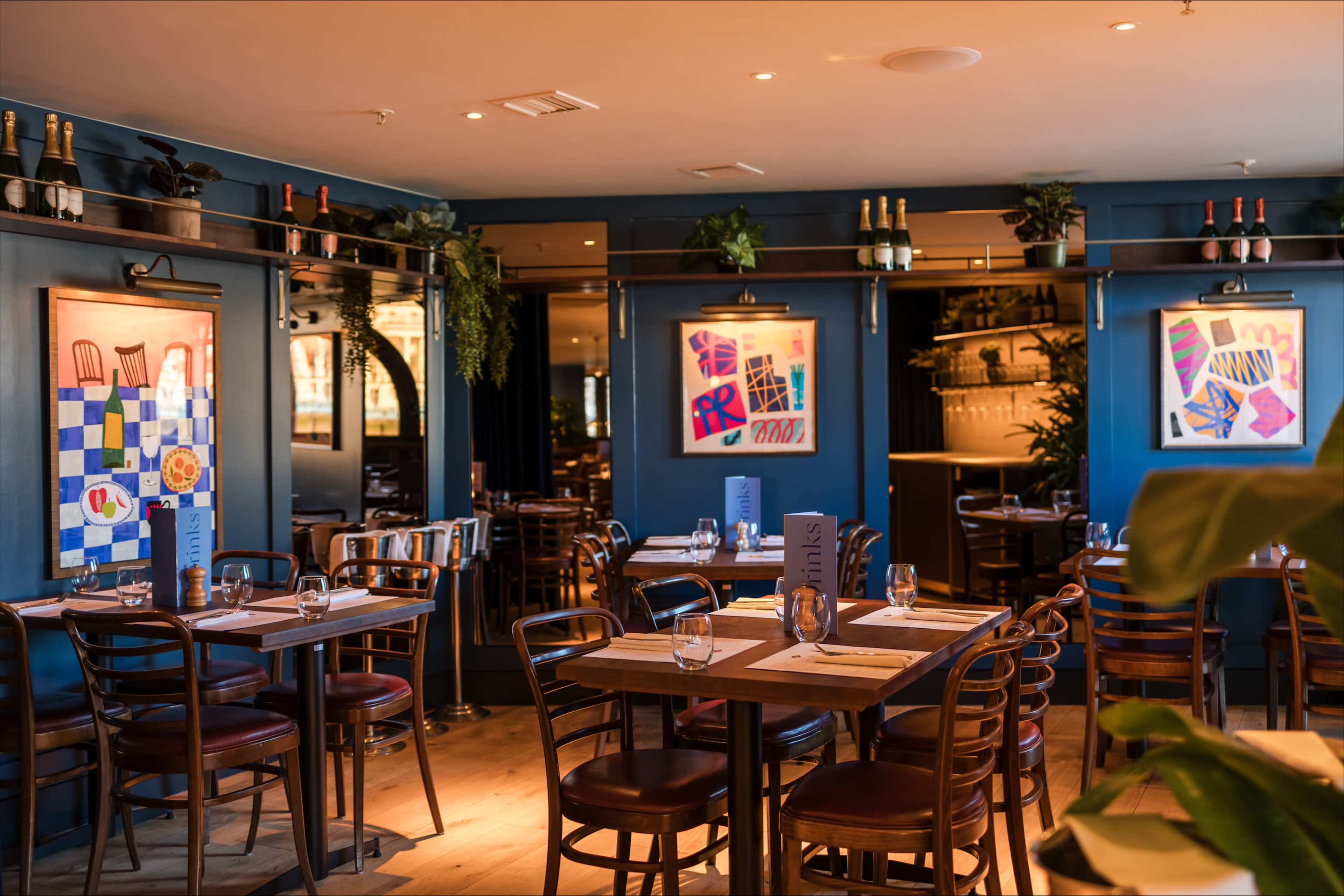 The image shows a well-decorated restaurant with wooden tables, chairs, and colorful artwork on the walls.