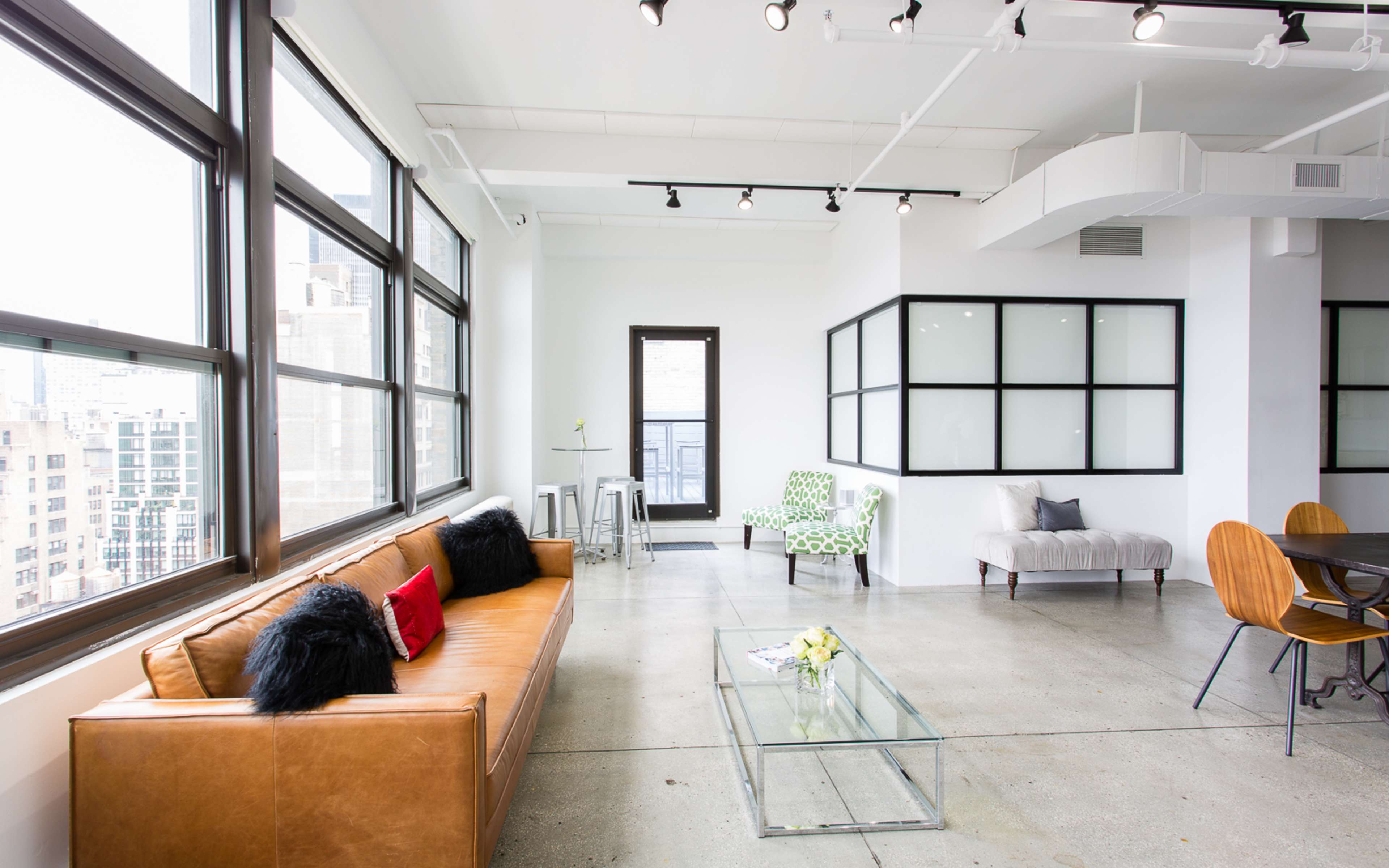 A modern, open-concept lounge area featuring large windows, a brown leather sofa, and contemporary furniture arrangements.
