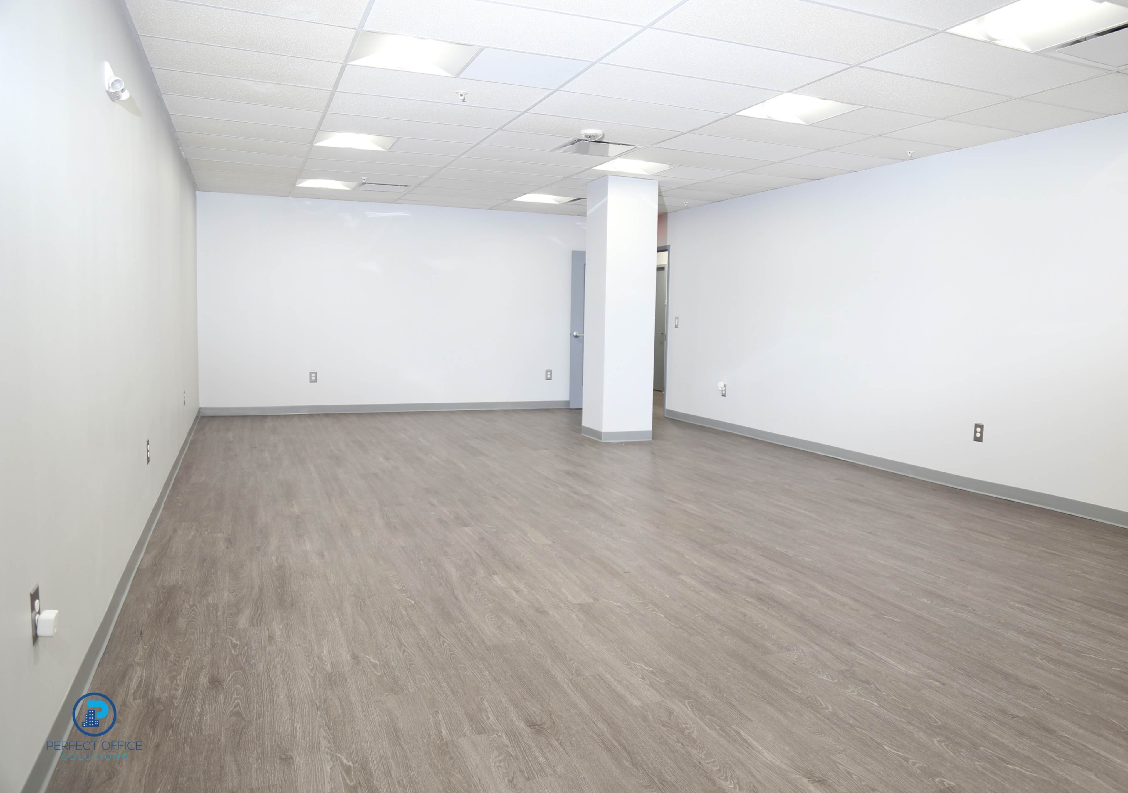 An empty, unadorned room with light-colored flooring and plain walls.