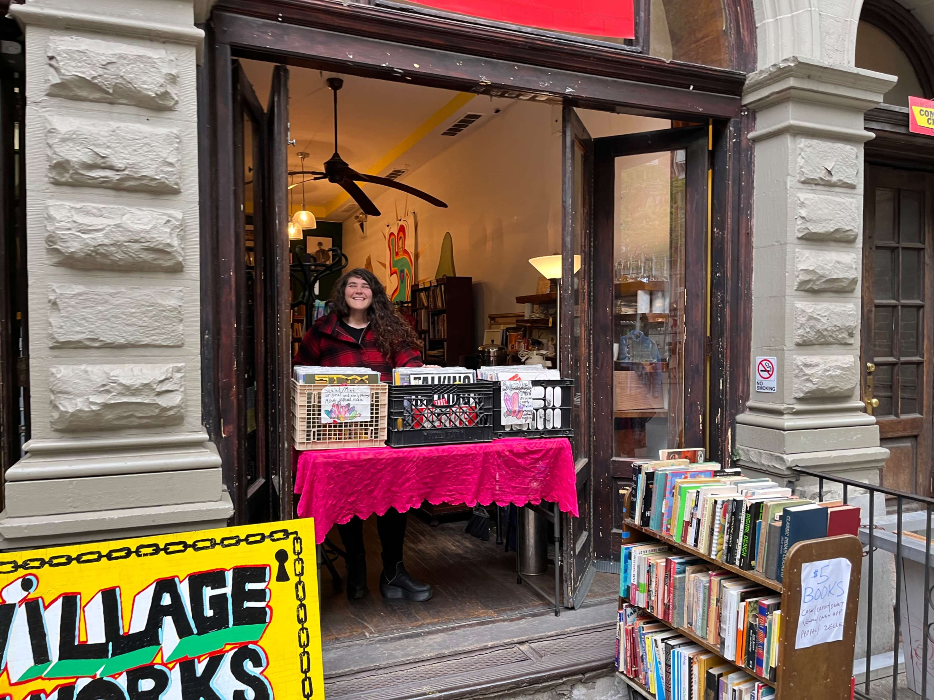A woman stands at the entrance of a bookstore, surrounded by books displayed on stands and tables.