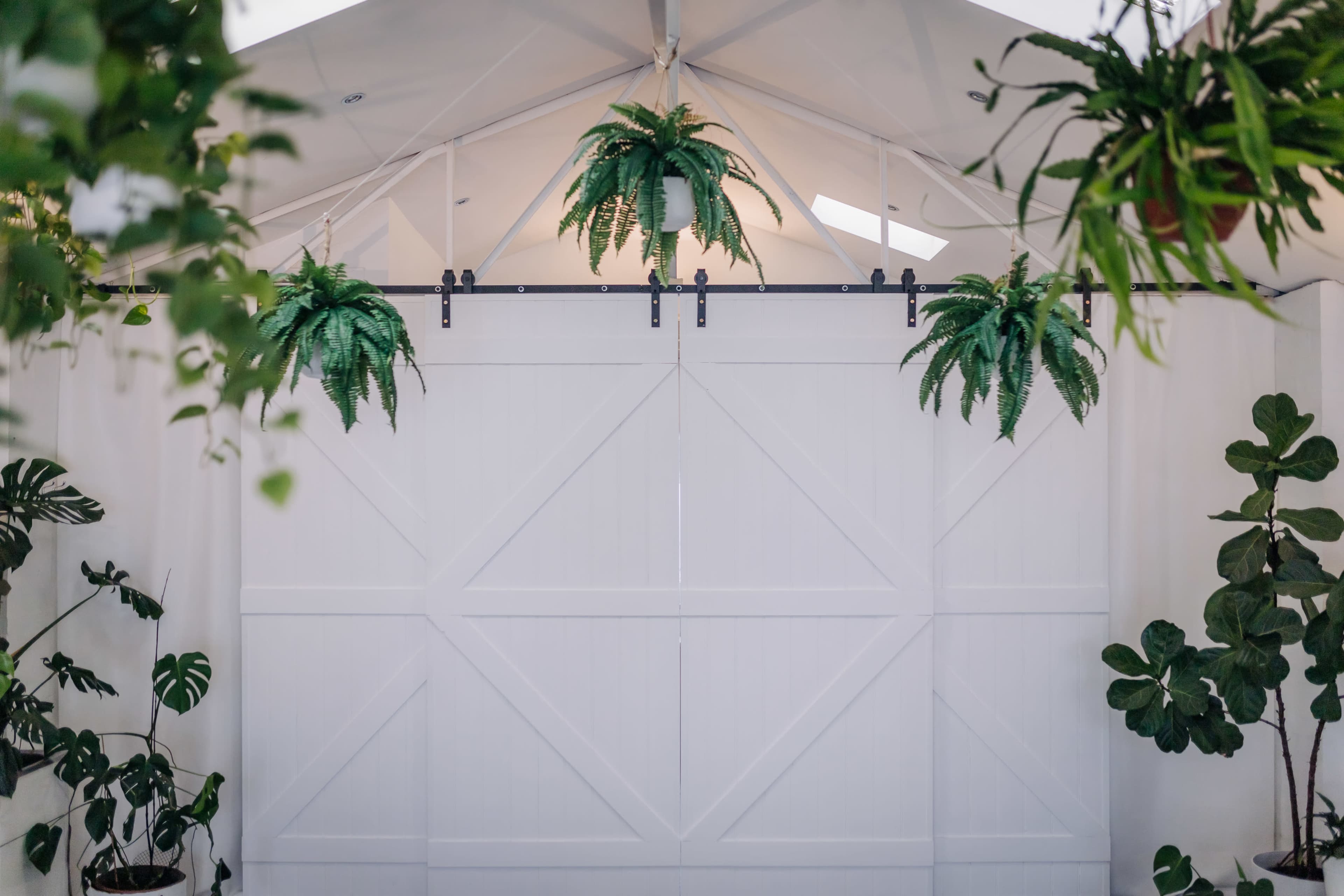 A white sliding barn door with greenery hanging above is featured in a bright, indoor space.