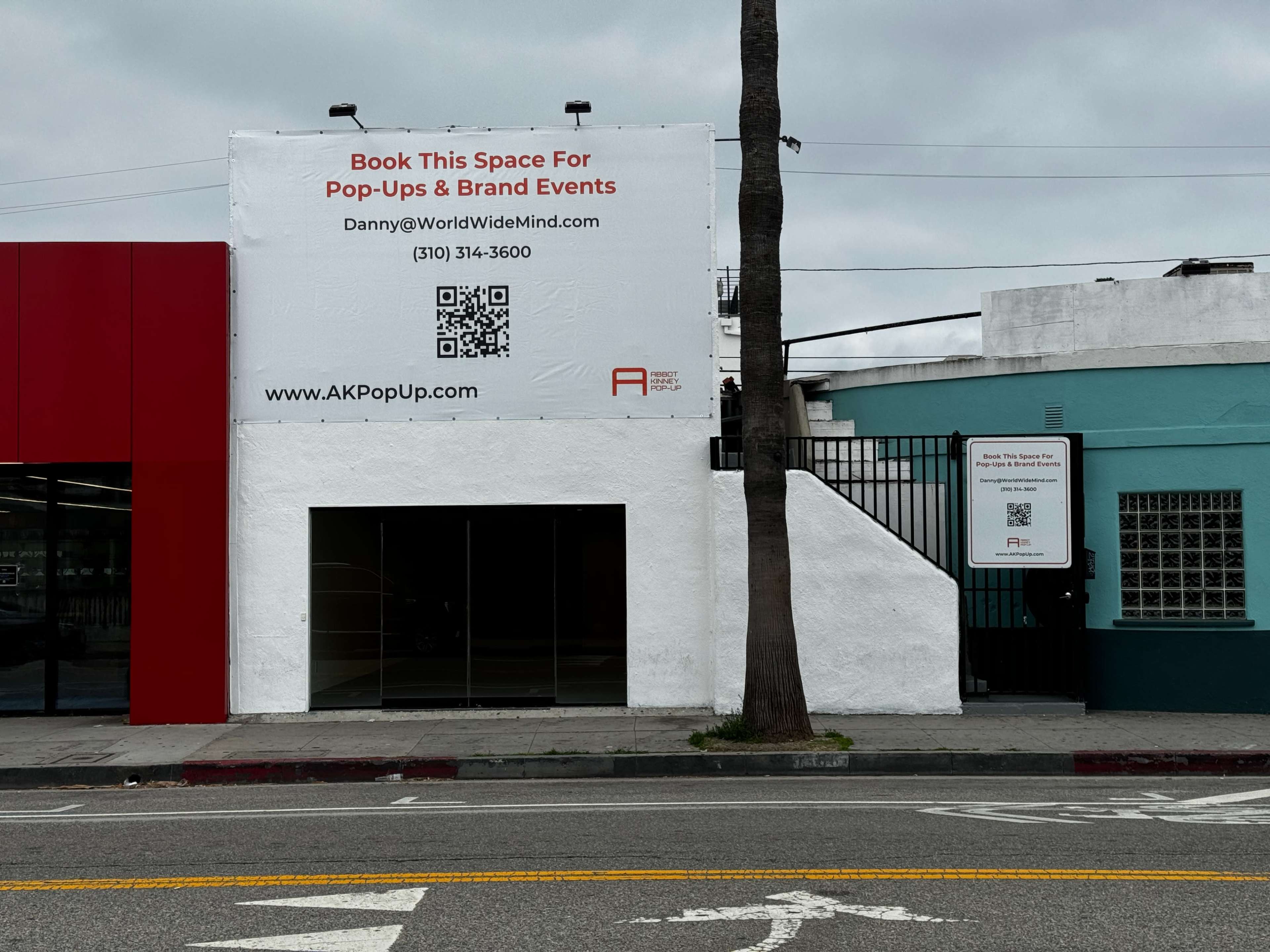 A building with a white exterior features a large sign advertising booking space for pop-ups and brand events, along with contact information and a QR code.