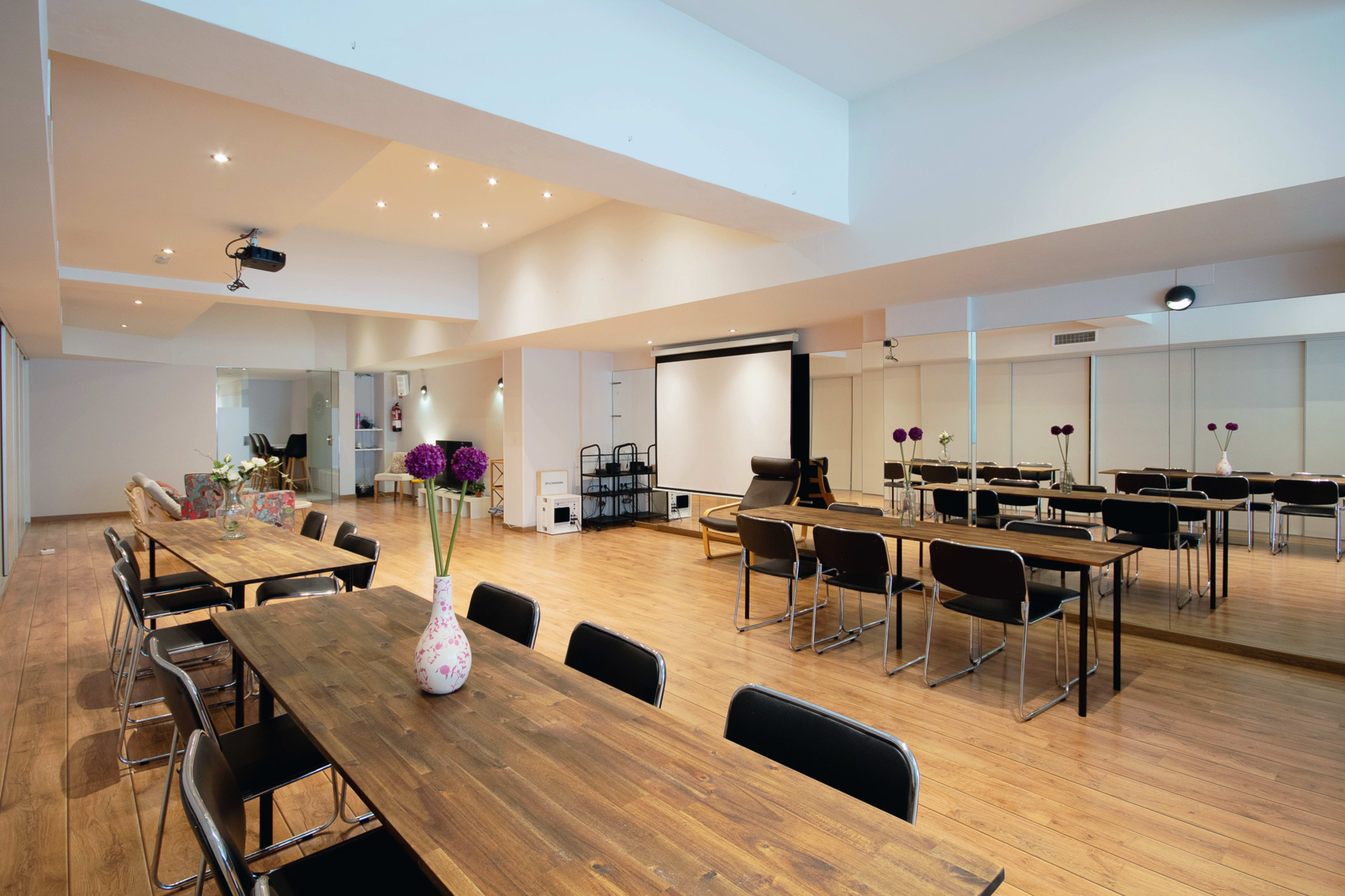 A spacious conference room features long wooden tables, black chairs, and a projection screen.
