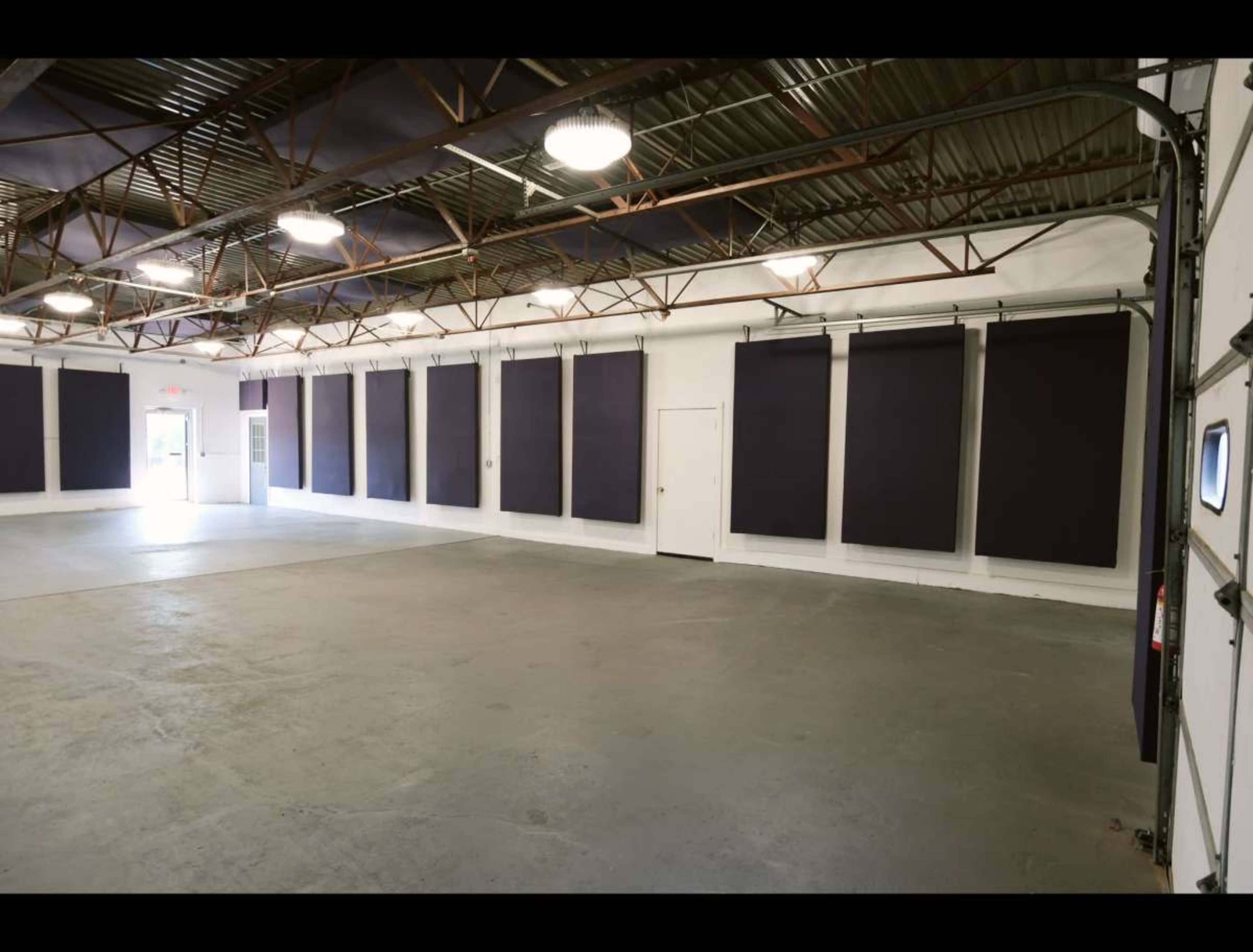 The image shows an empty indoor space with a concrete floor, white walls, and large dark panels hanging from the ceiling.