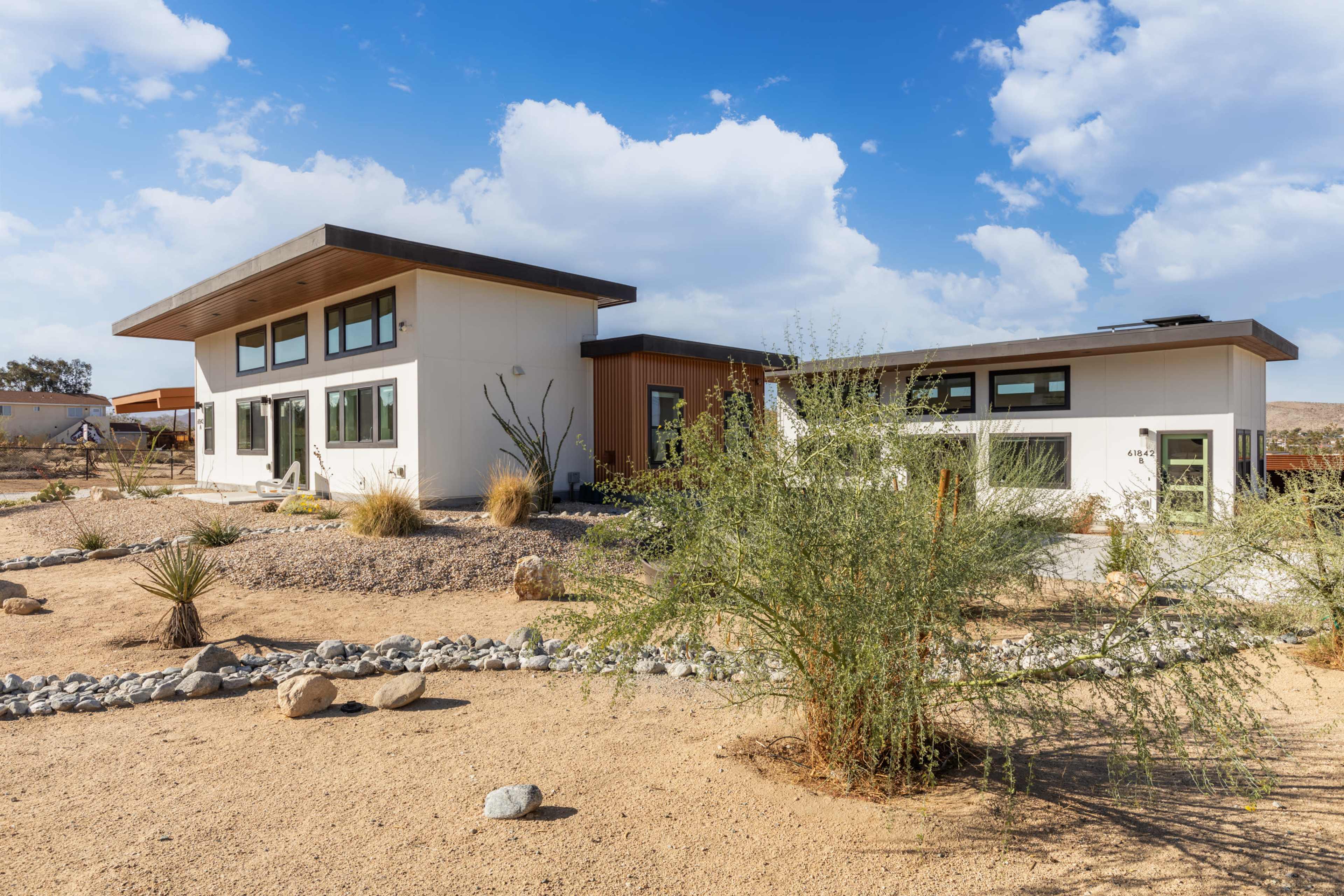 A modern house with large windows is situated in a desert landscape featuring gravel and drought-resistant plants.