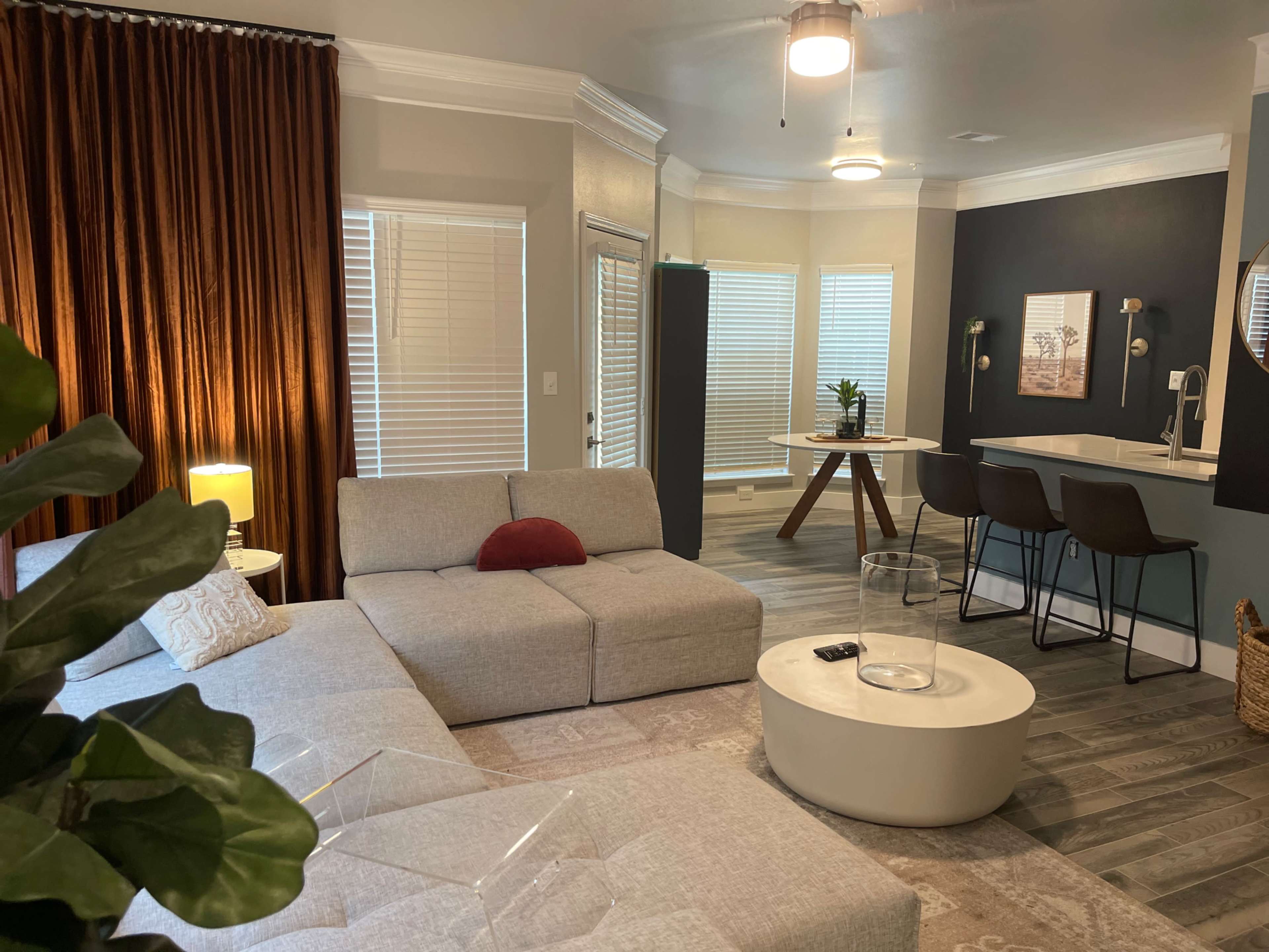 A modern living space featuring a gray sectional sofa, a round coffee table, and a dining area with a small table and chairs near large windows.