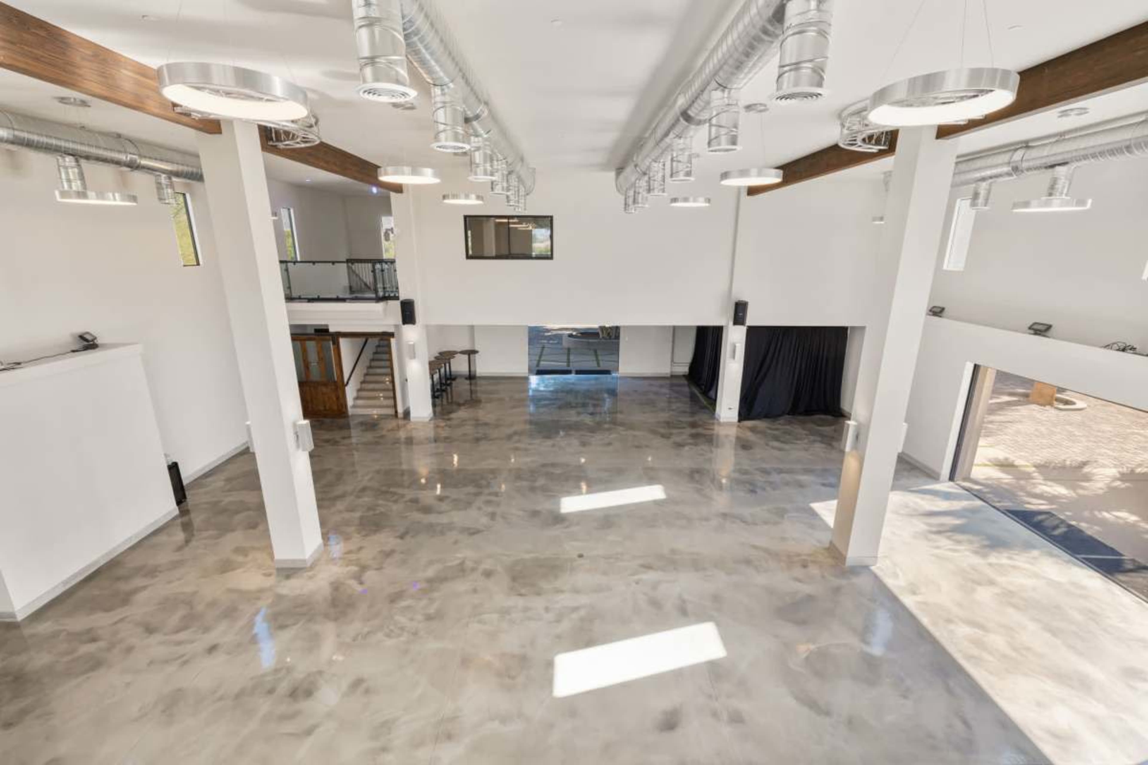 The image shows a spacious, modern interior of a venue with polished concrete floors, high ceilings, and large windows.