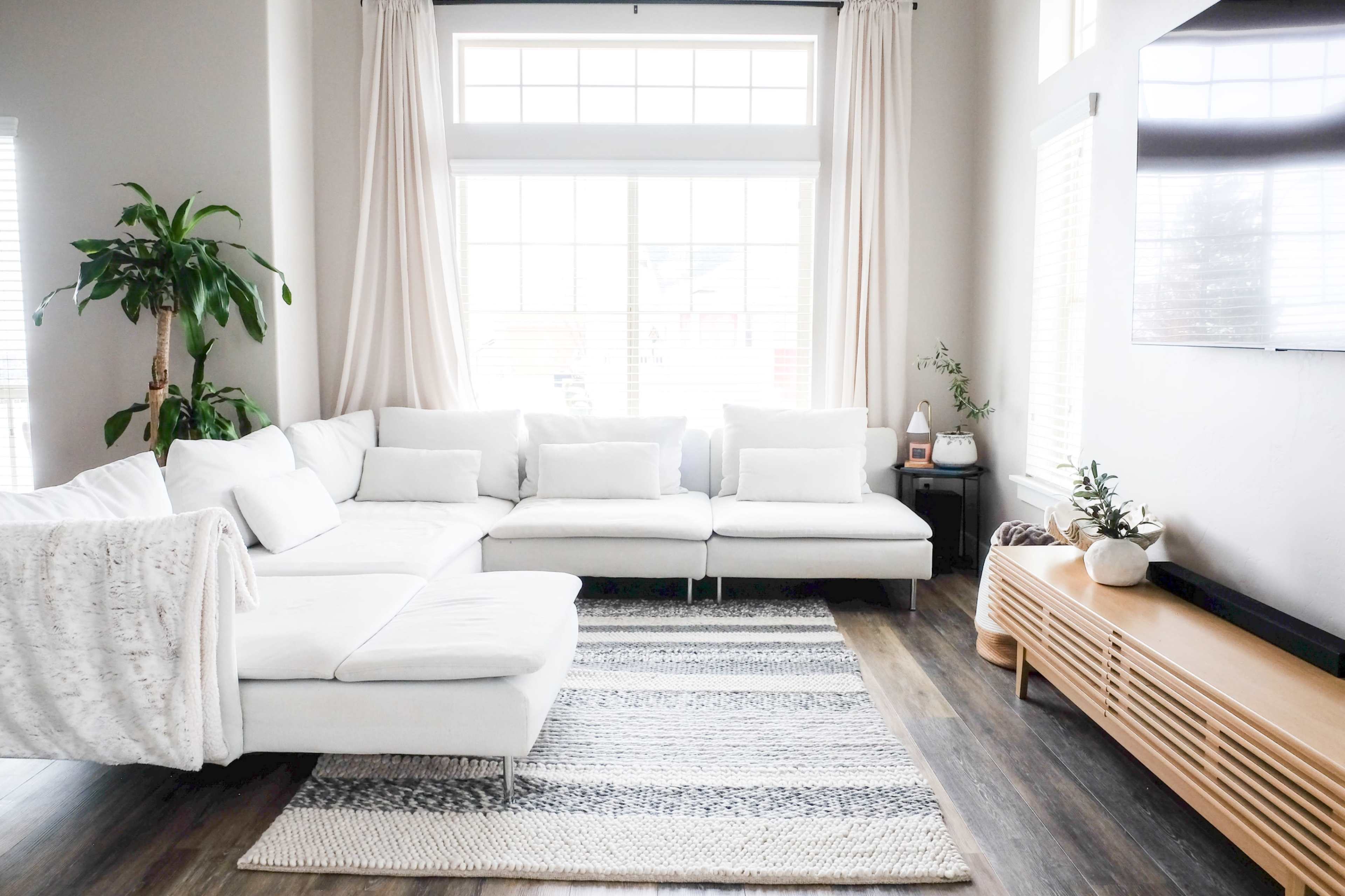 A spacious living room features a white sectional sofa, a striped area rug, and large windows with natural light streaming in.